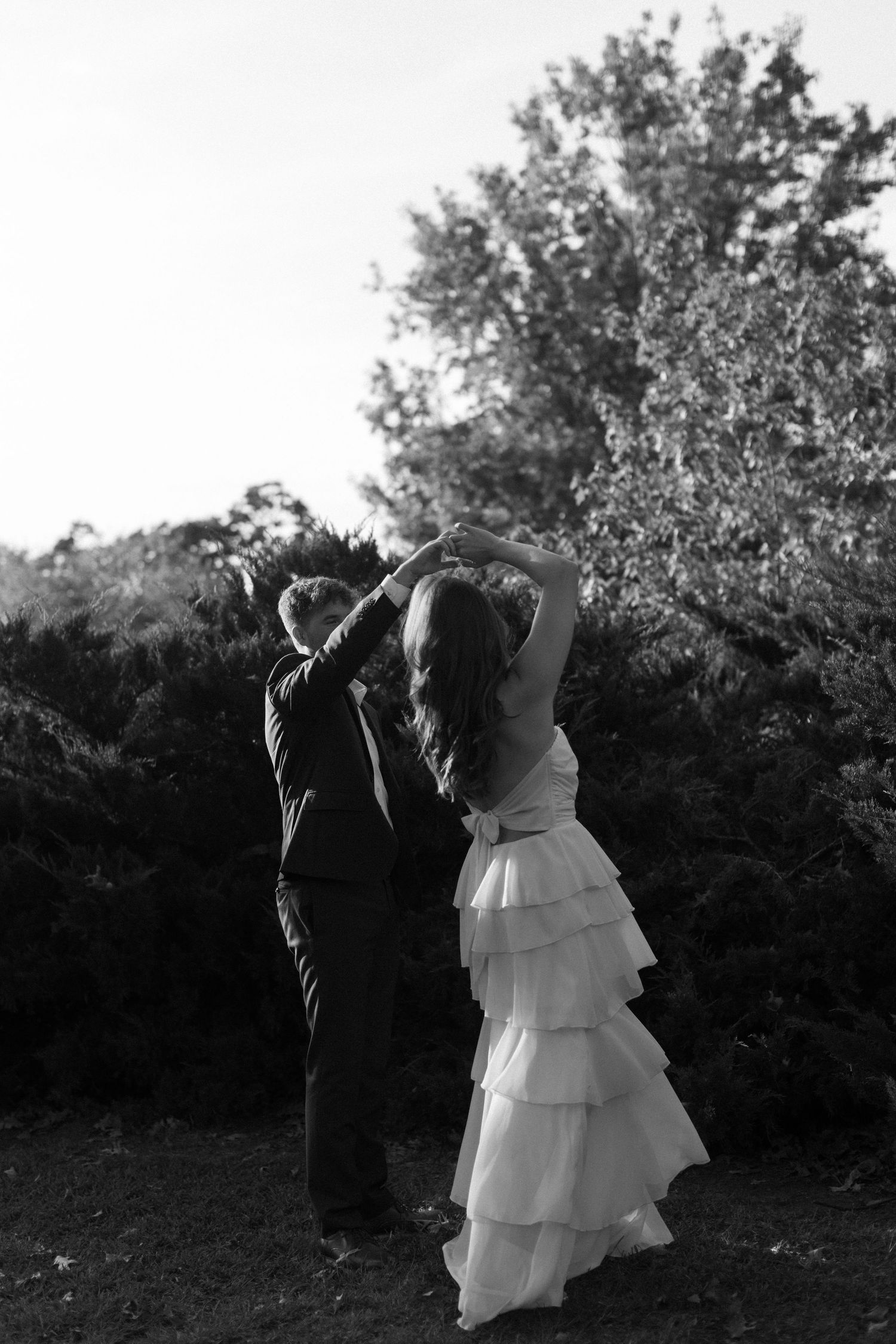 A couple shares playful dance moves outdoors in black and white photography.