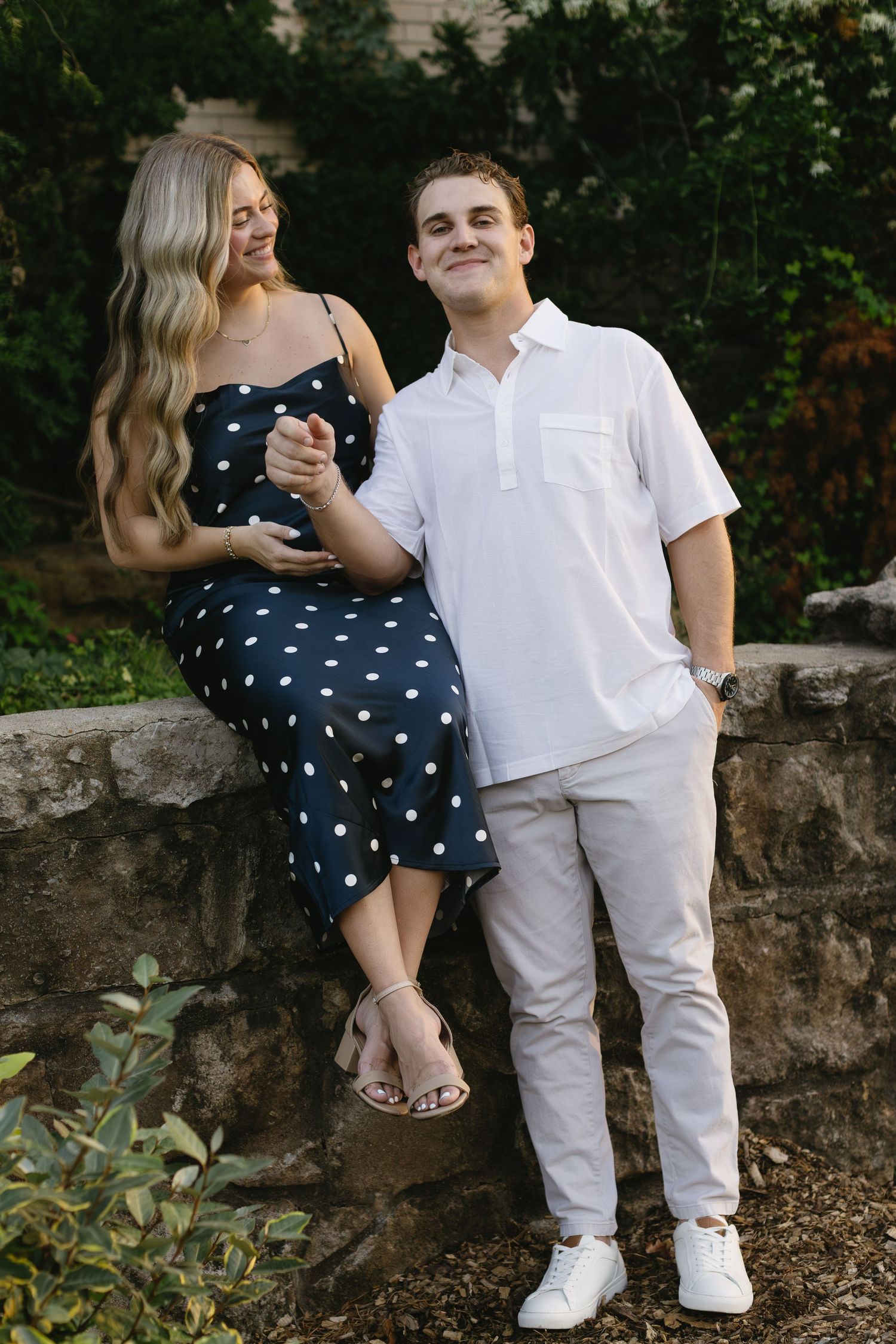 A couple sitting on a stone wall sharing intimate moments outdoors, wearing white and polka dots.