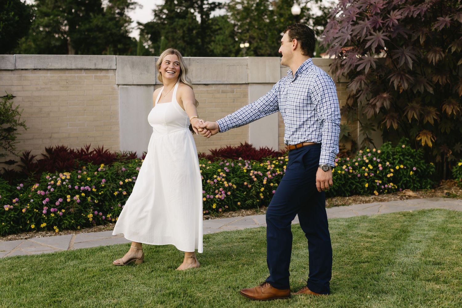 A couple dances together in a garden outside on a summer day, the bride wearing a flowing white dress.