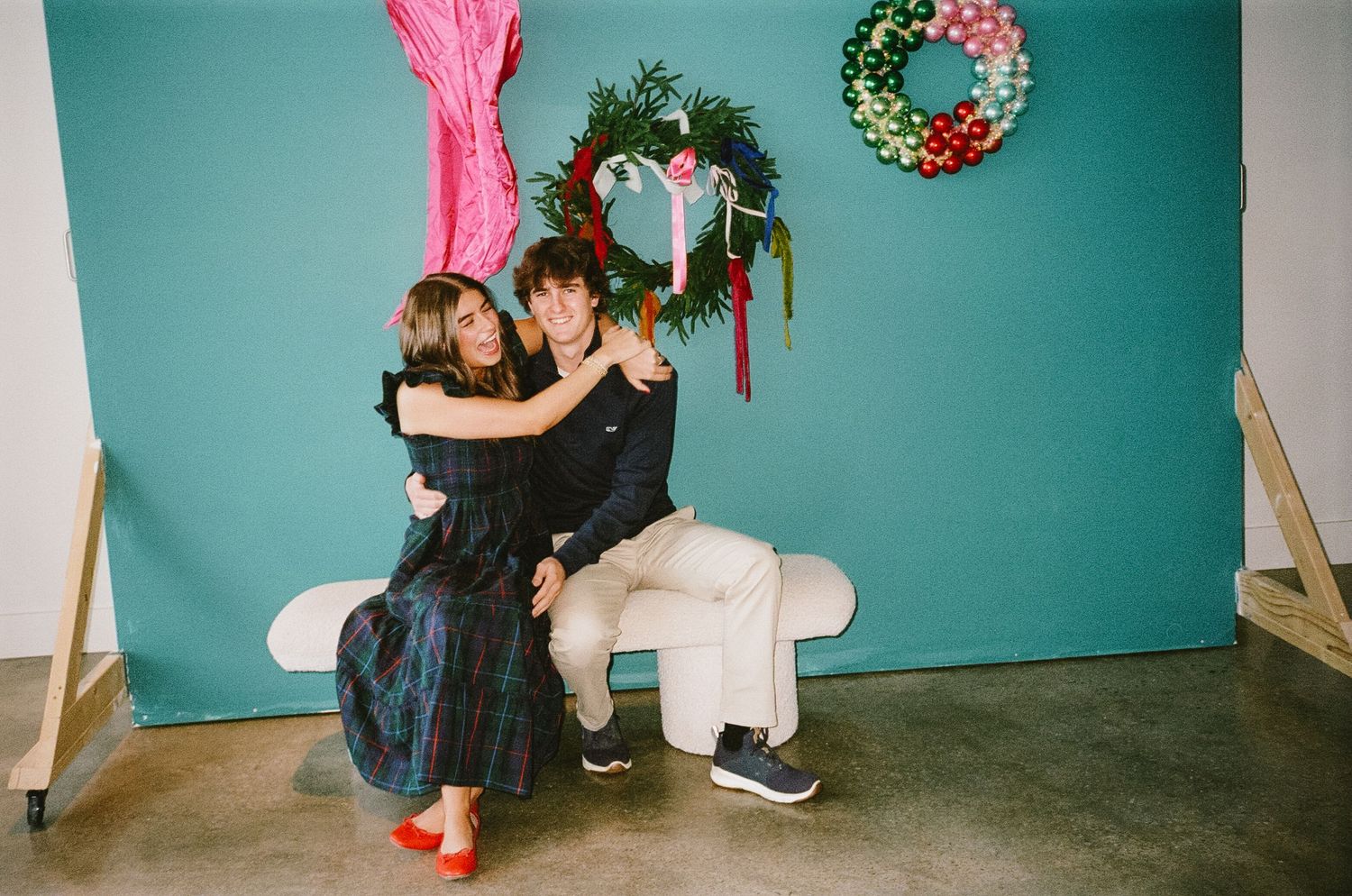 A couple dances intimately in front of a turquoise wall with a holiday wreath decoration visible in the background.