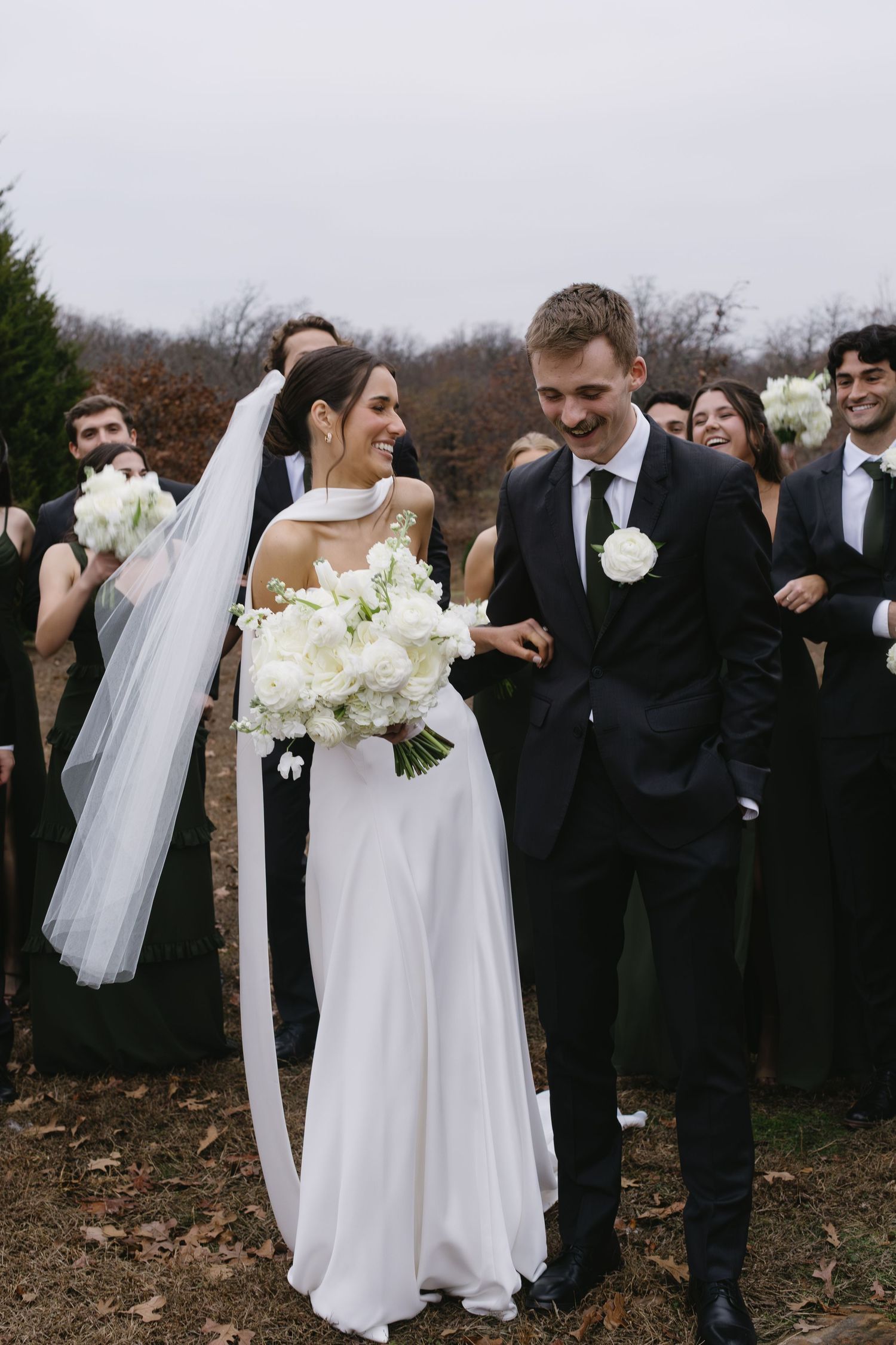 Wedding party in black and white attire celebrating outdoors during autumn.