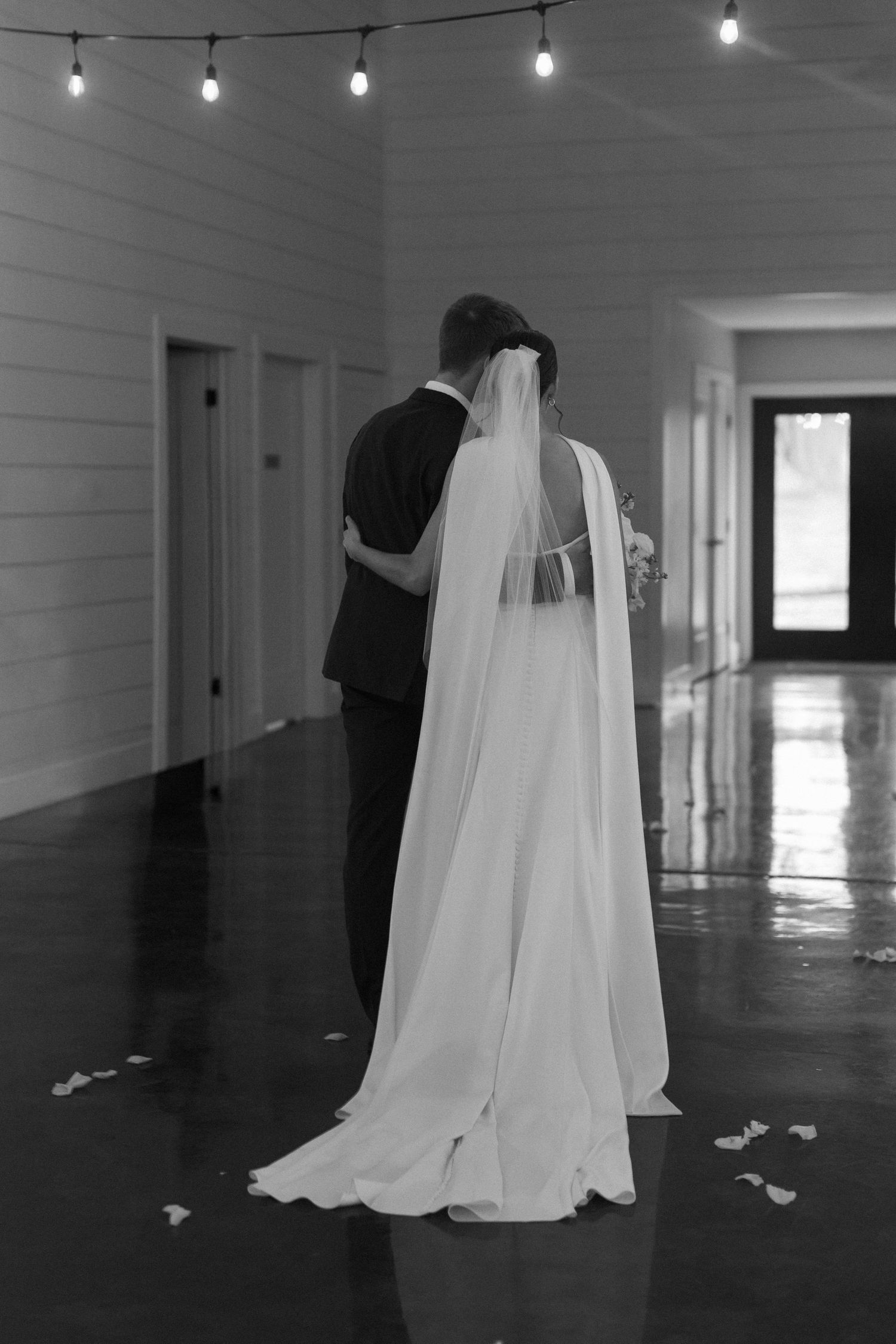 Minimalist indoor venue with string lights and flowing white wedding dress silhouette against dark floor.