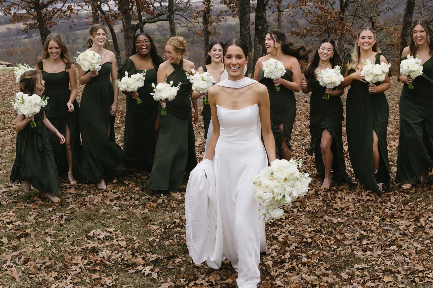 Wedding party poses in autumn setting with bridesmaids wearing black dresses and bride in white gown.