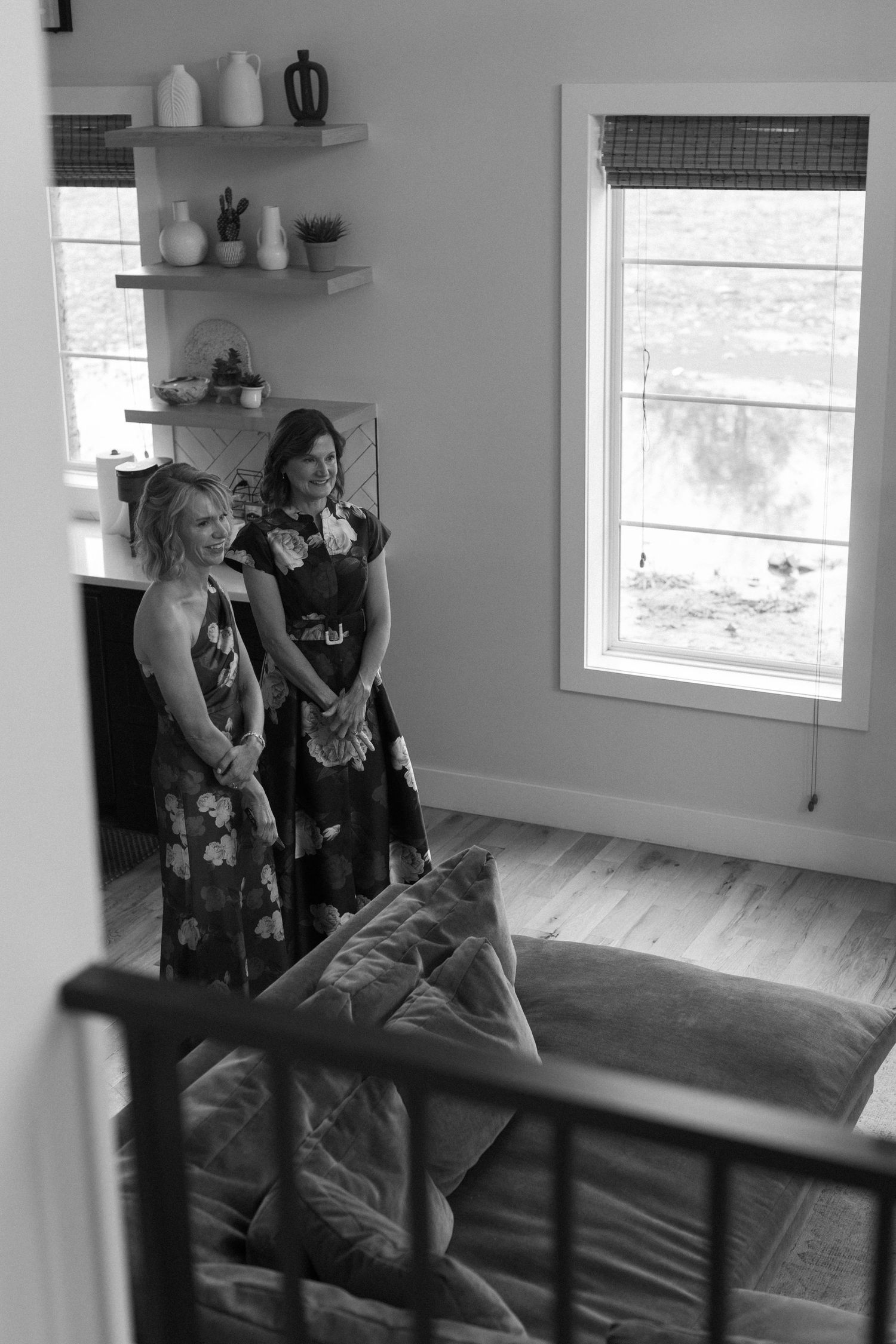 Black and white photo of people sitting in a modern living room with windows and shelving.