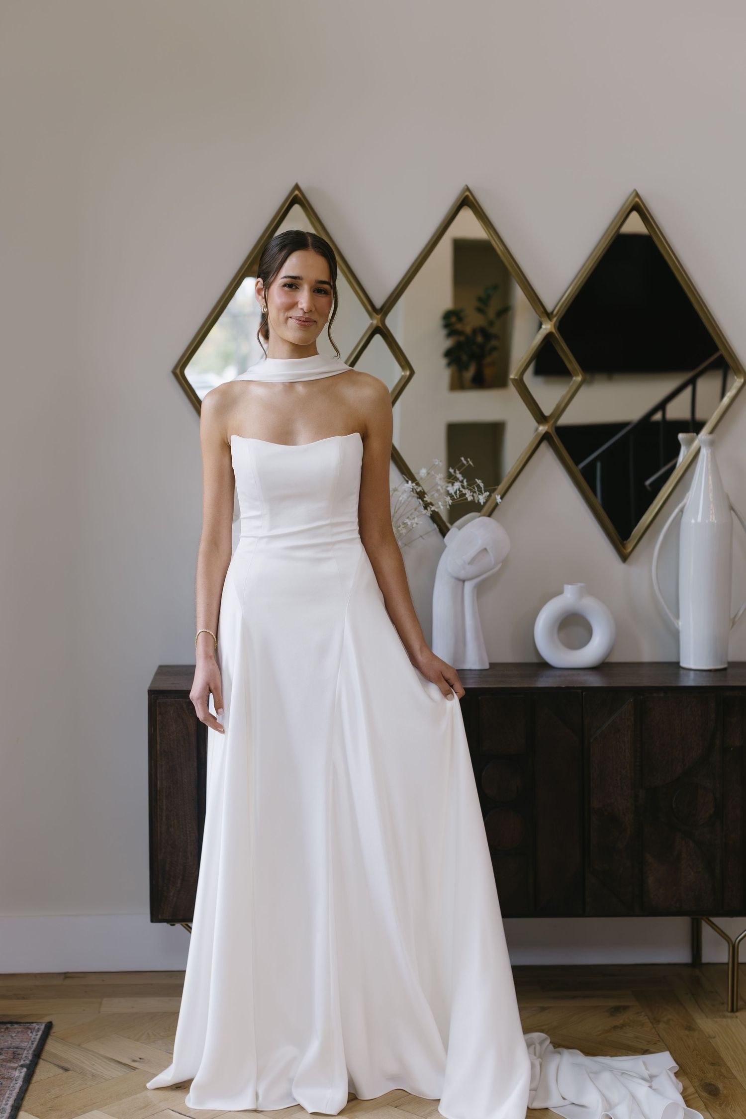 Modern white wedding gown displayed in a room with geometric mirrors and contemporary decor.