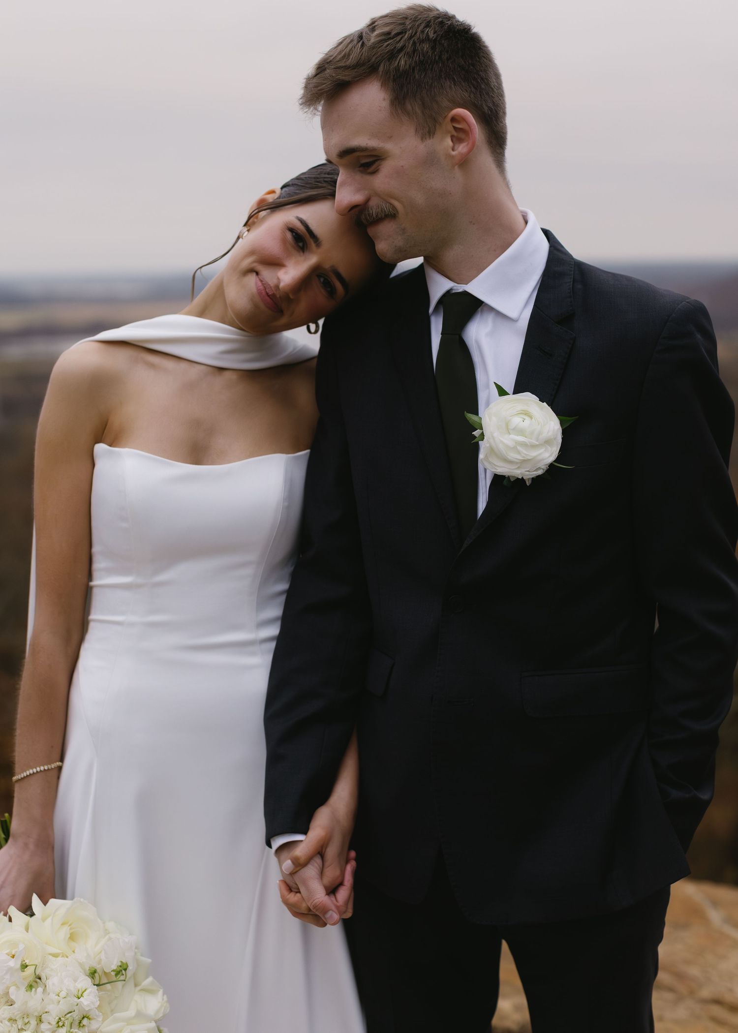 Romantic portrait of couple in wedding attire against misty landscape backdrop.