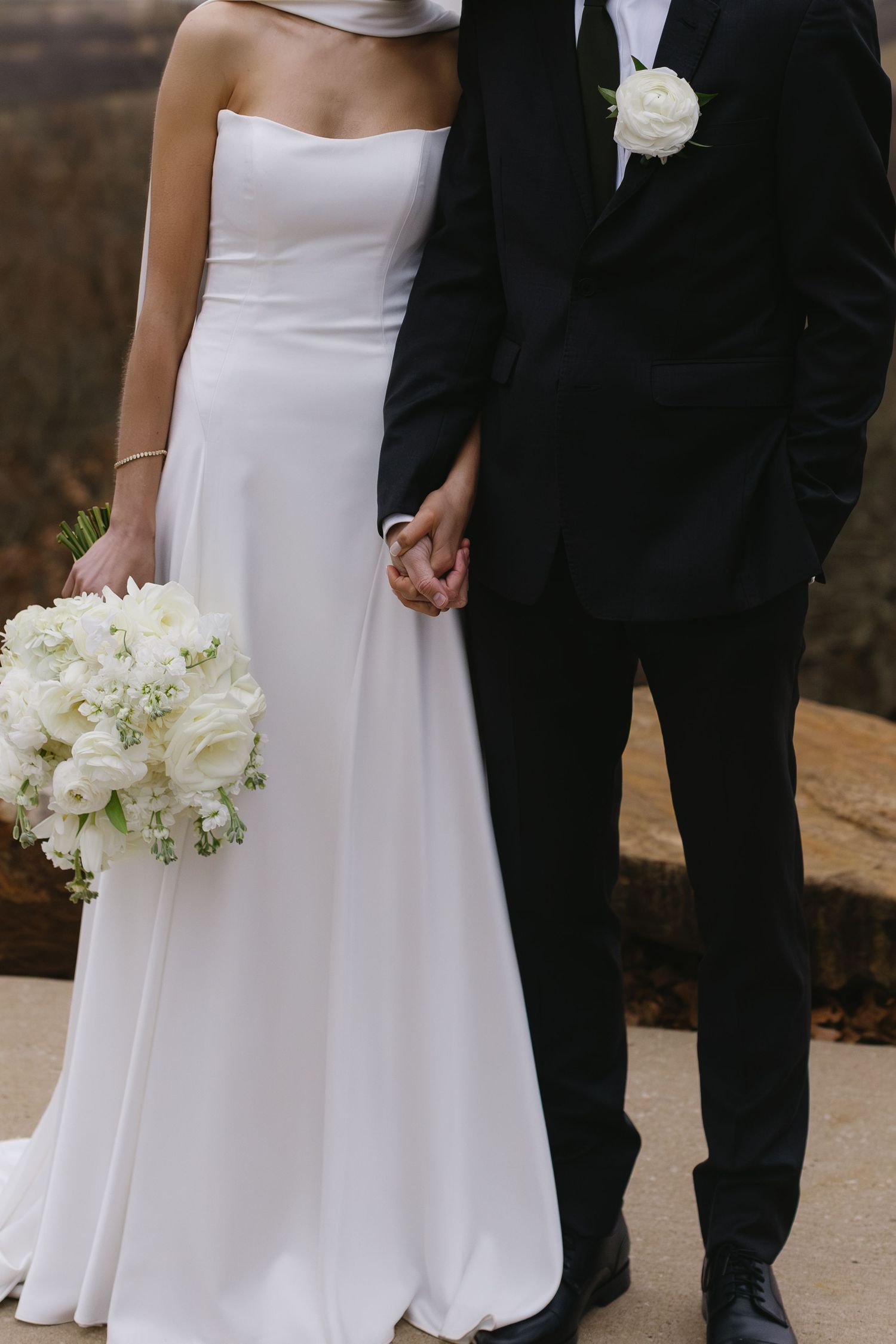 Elegant wedding couple poses together with white bouquet against autumn backdrop.