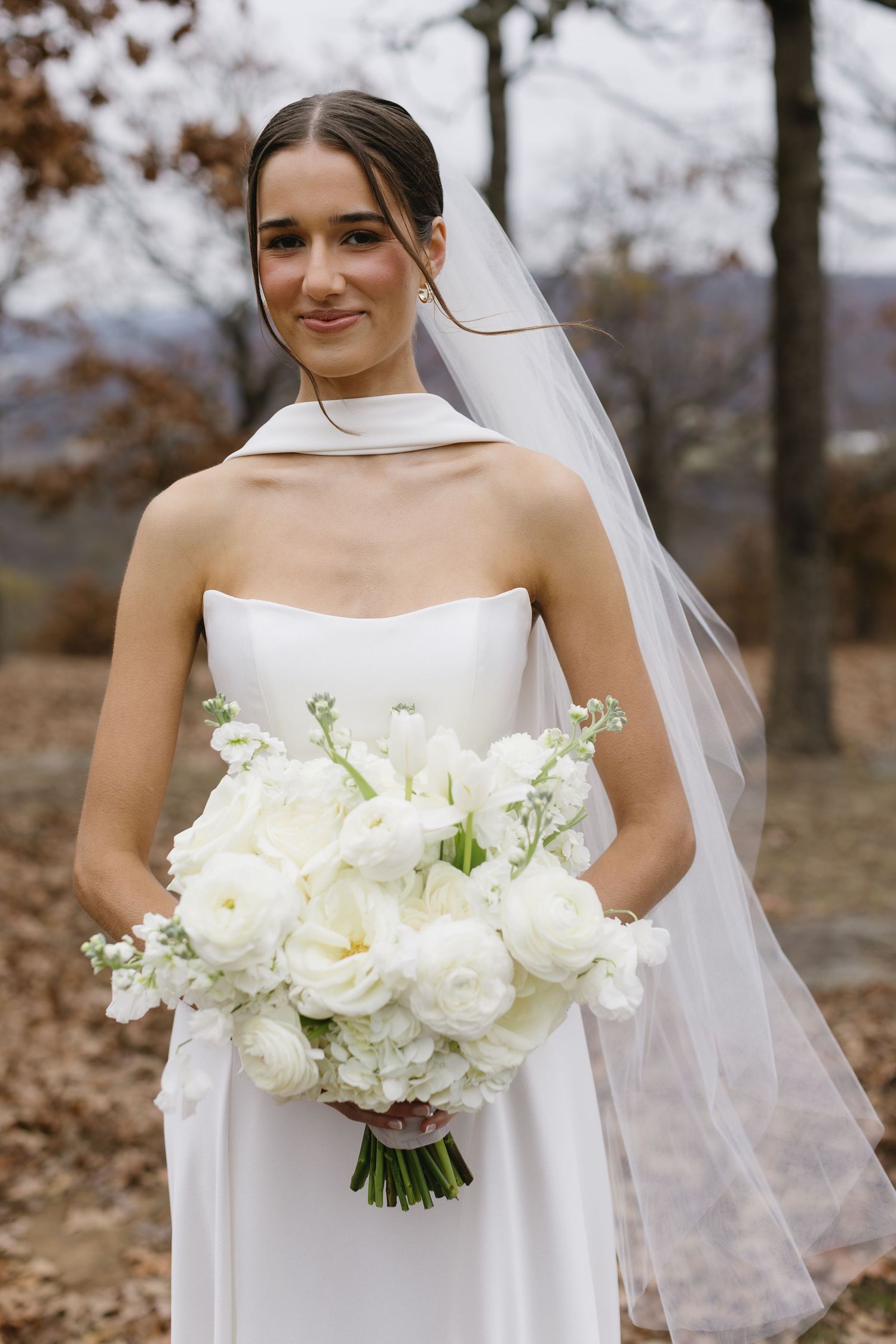 Bride holding classic white rose bouquet in elegant wedding dress with sheer veil.