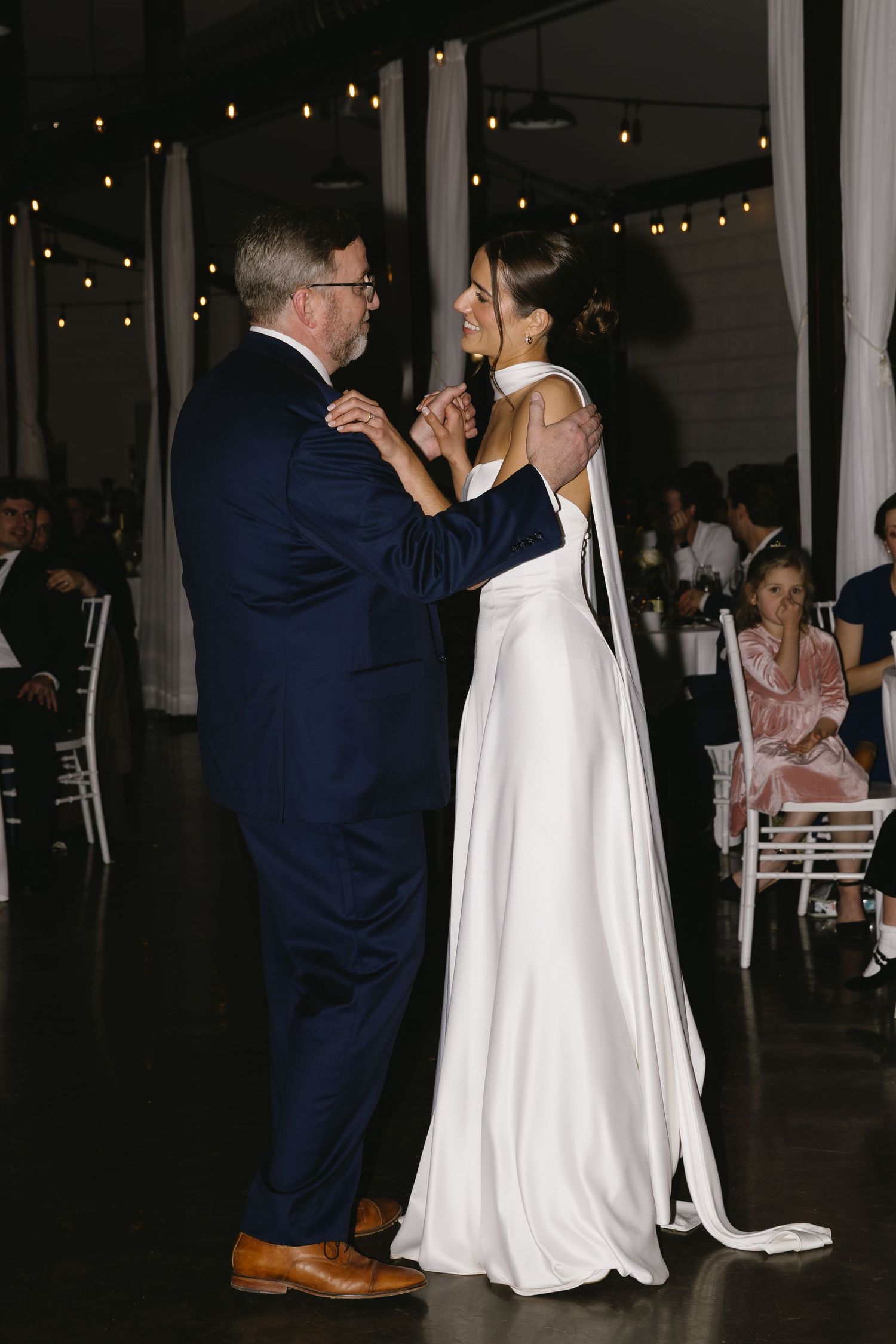 Wedding guests dancing in formal attire under romantic string lighting.