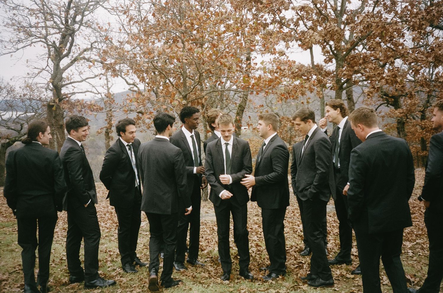 Groomsmen in black suits gathered in a circle during fall wedding.