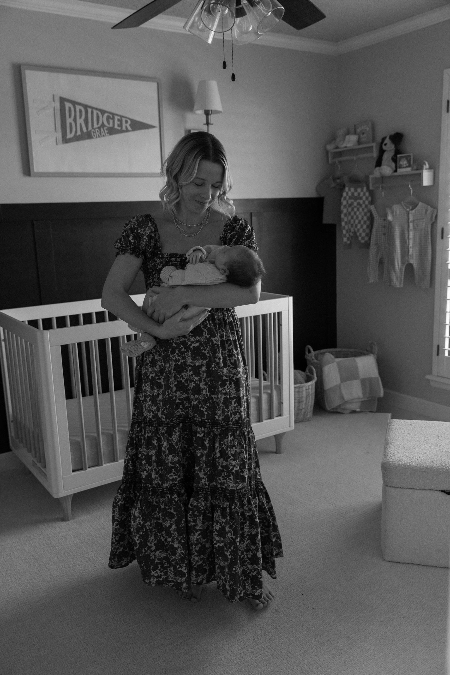 A nursery room with modern white crib, ceiling fan, and wall decor in gray tones.