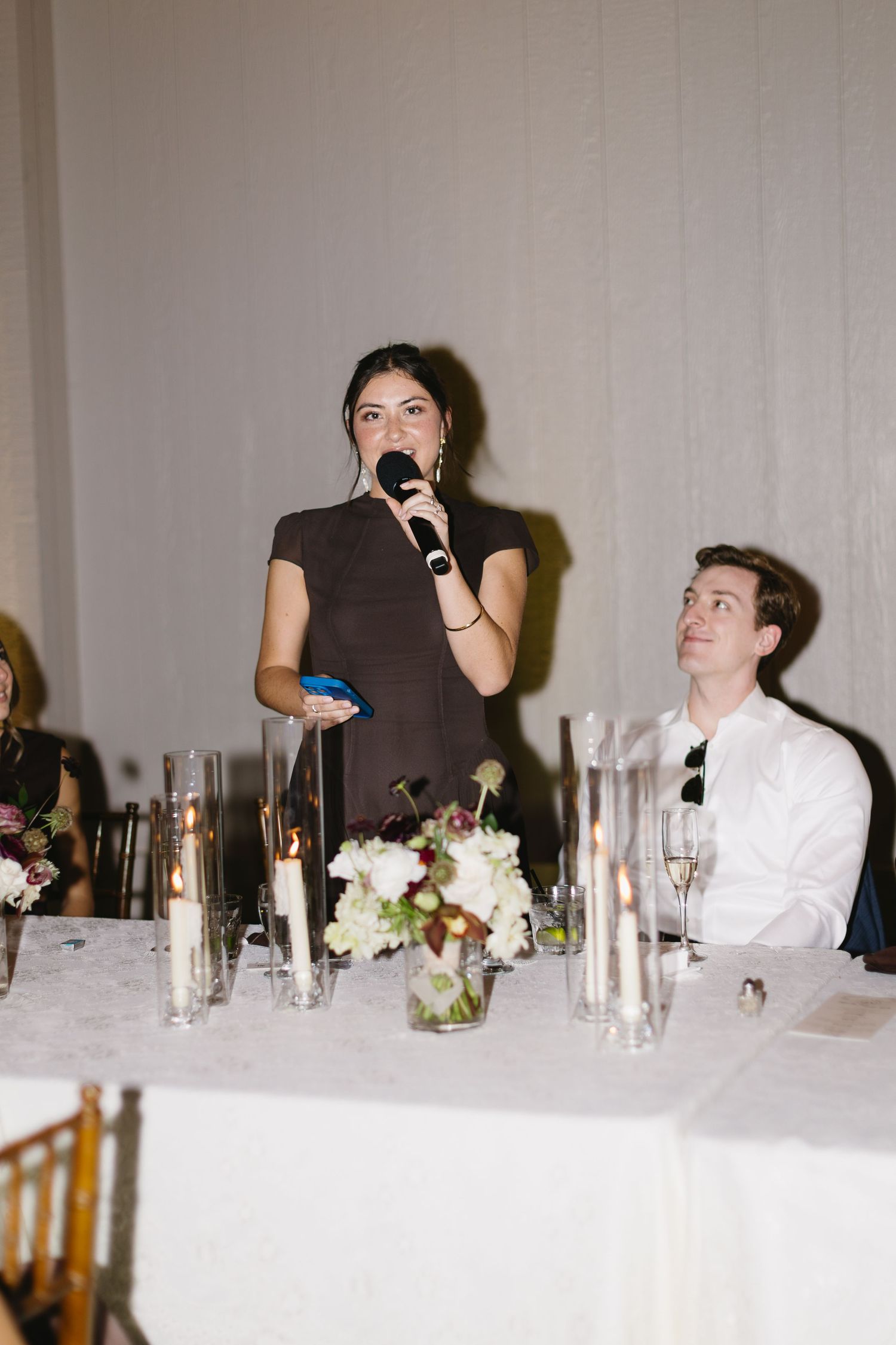 Wedding reception head table with white linens and floral centerpieces during speeches.