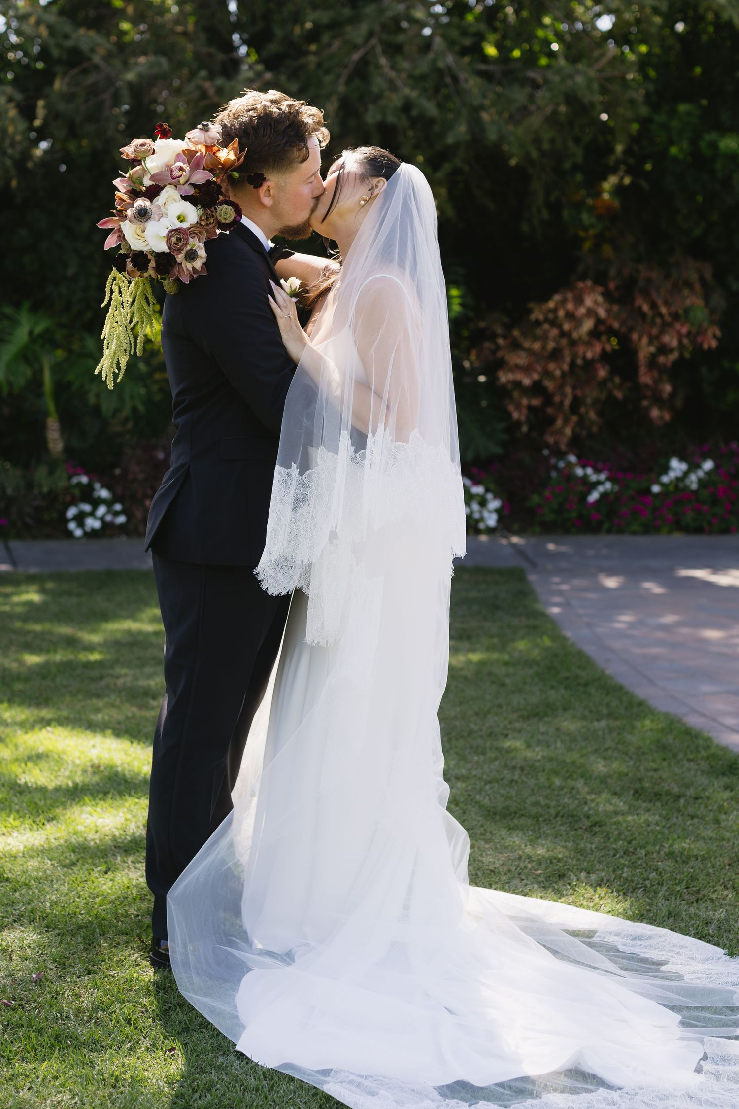 Newlyweds share an intimate moment on a sunlit garden pathway.