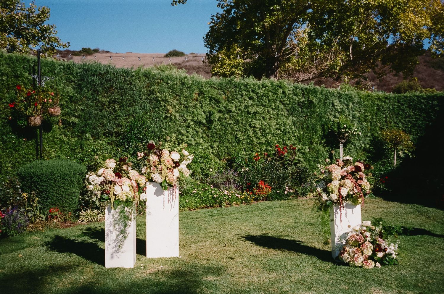 Outdoor wedding ceremony setup with white floral arrangements and chairs on a grassy hillside during golden hour.