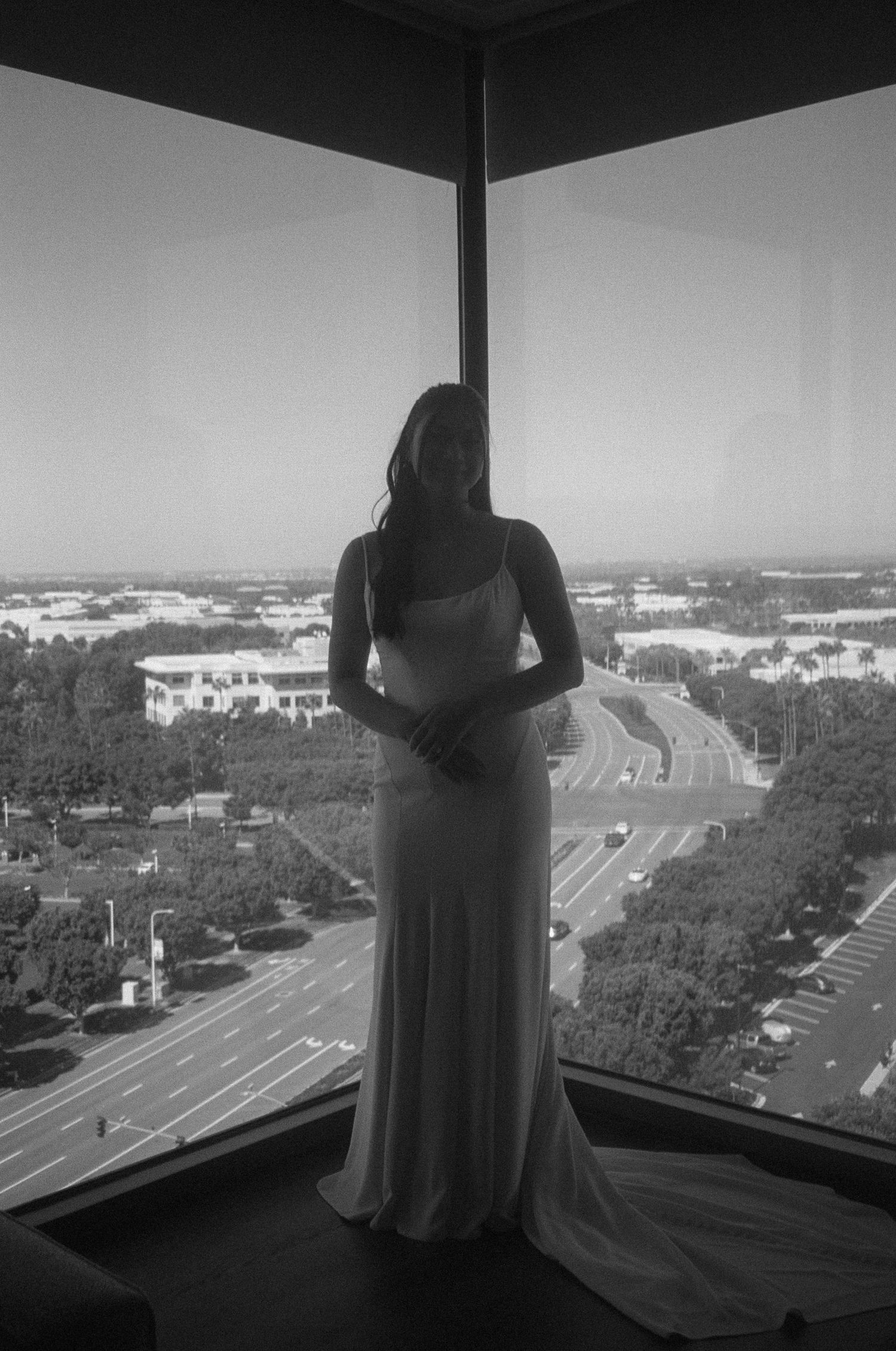 A silhouetted figure stands at a window overlooking a cityscape with parking lots below.
