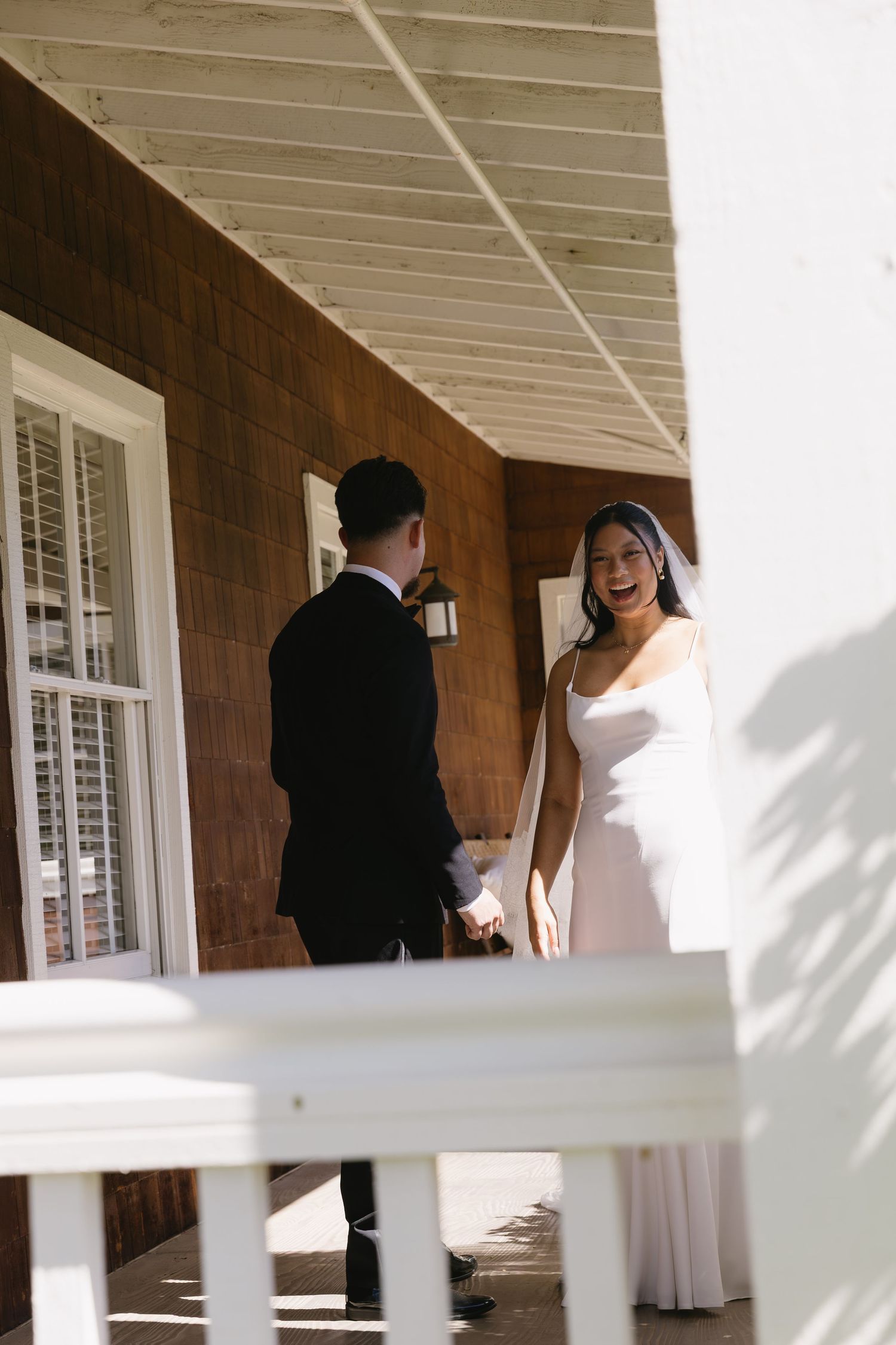 A wedding first look moment captured through white porch railings in natural light.