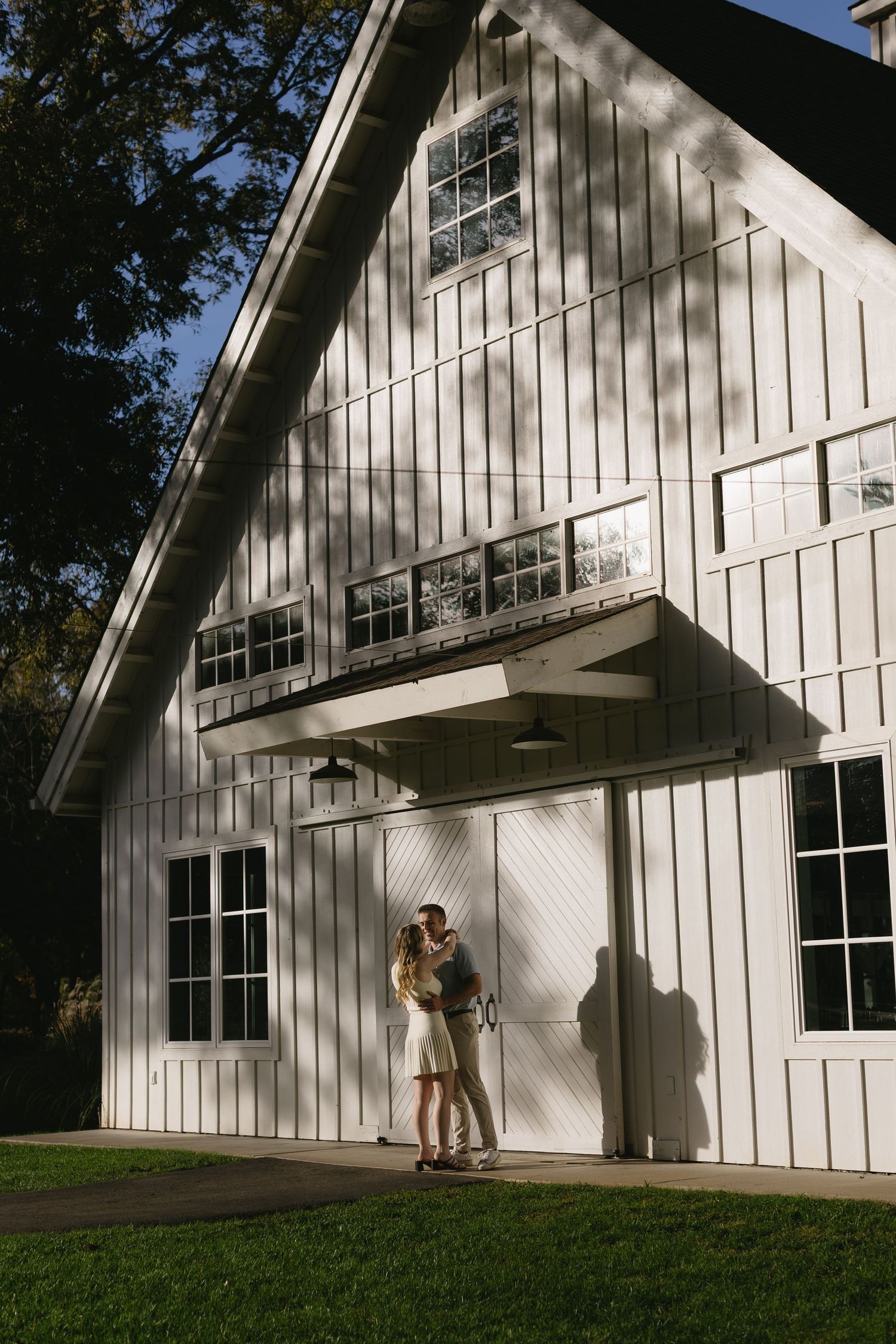 A modern white barn-style building with large windows photographed from different angles on a sunny day.