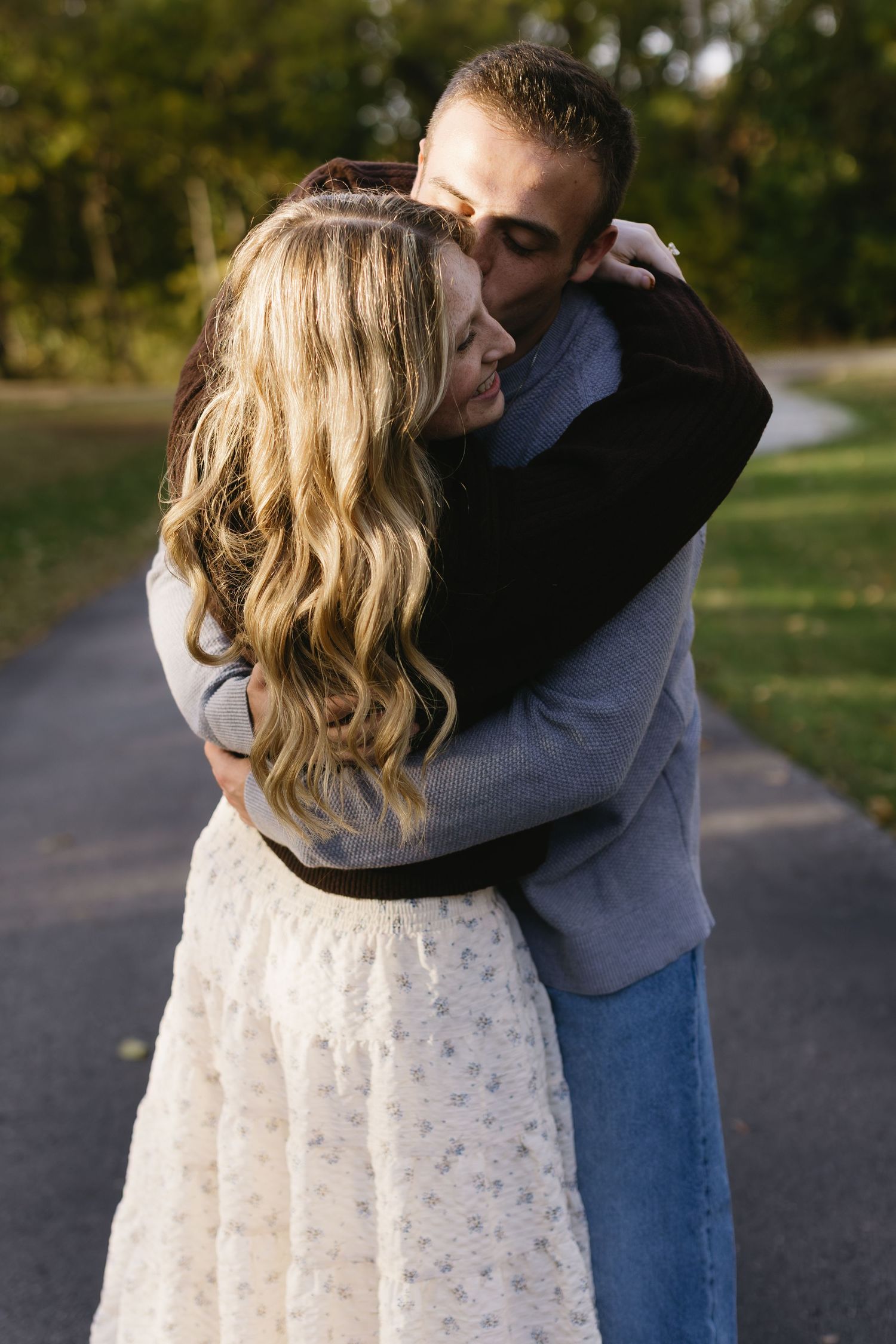 Romantic couple embracing in white dress and casual wear on autumn pathway.