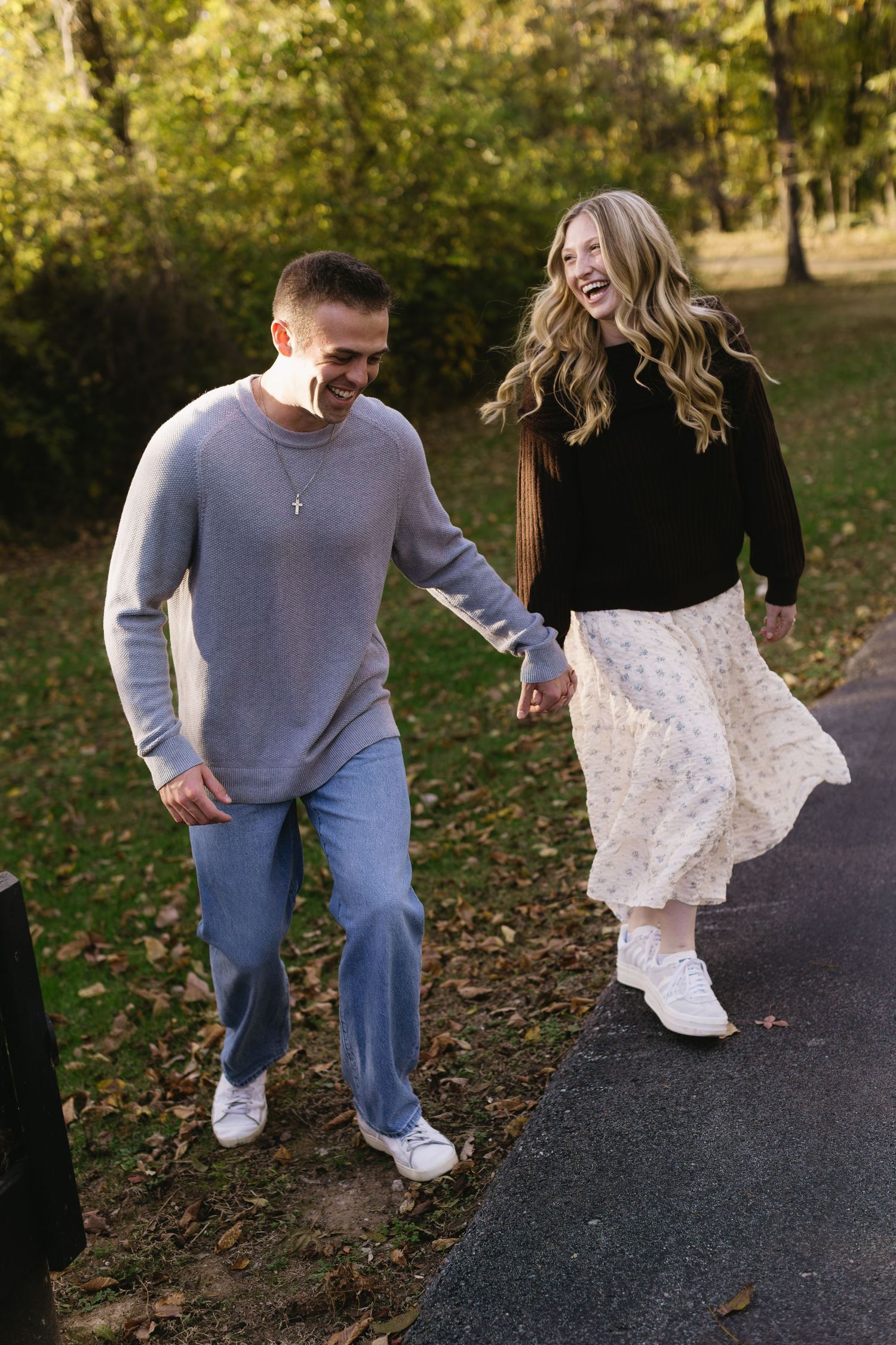 A couple dances and laughs together on a path surrounded by fall foliage.
