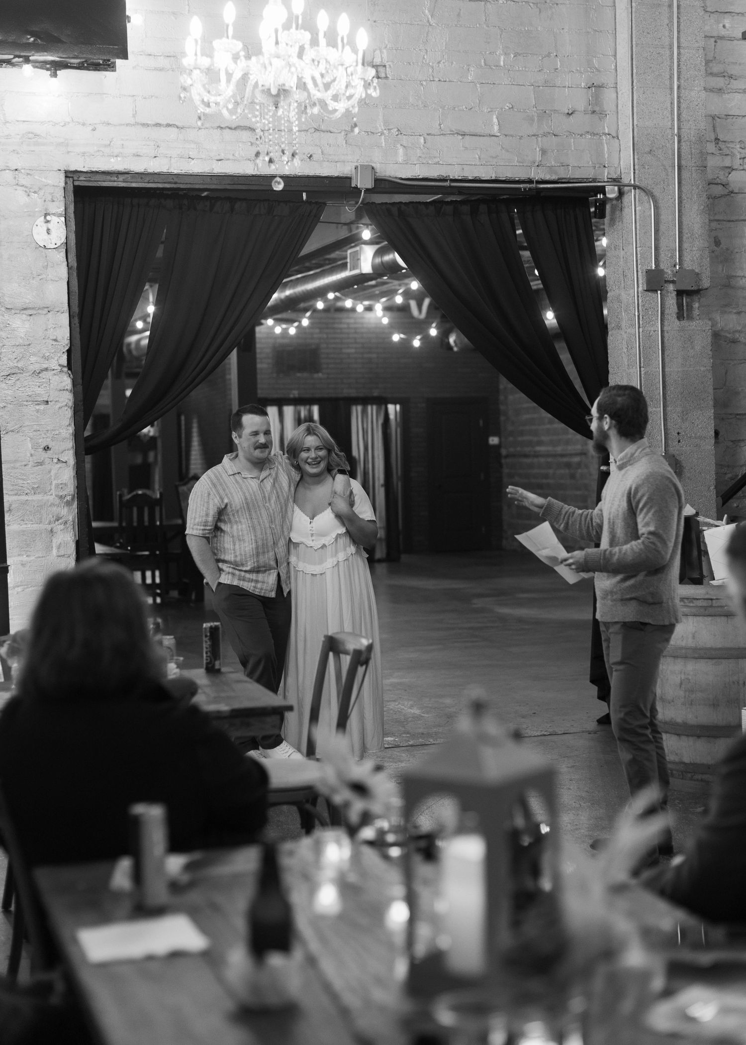 Indoor event space with chandeliers and dark curtains as guests gather for a celebration.