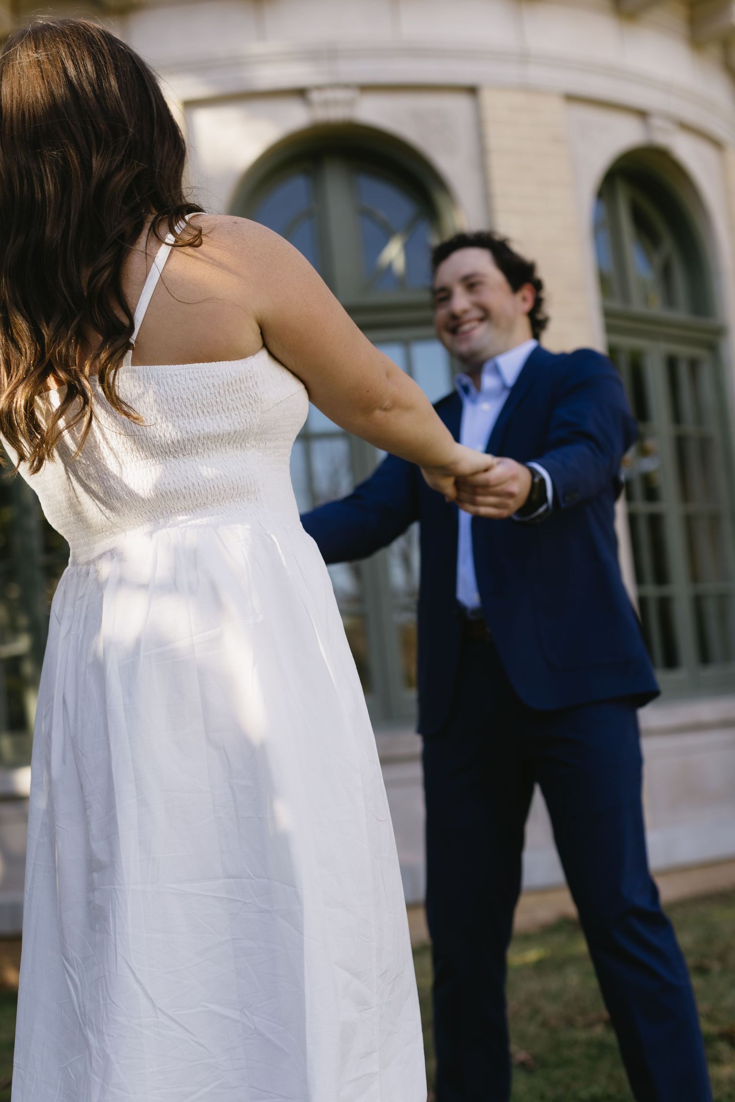 A playful moment of a couple dancing outside a building with arched windows.