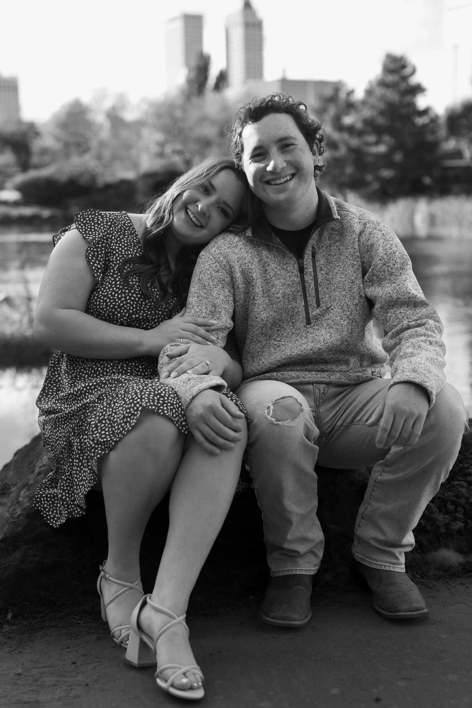 A black and white portrait of a couple sitting together with a city skyline in the background.