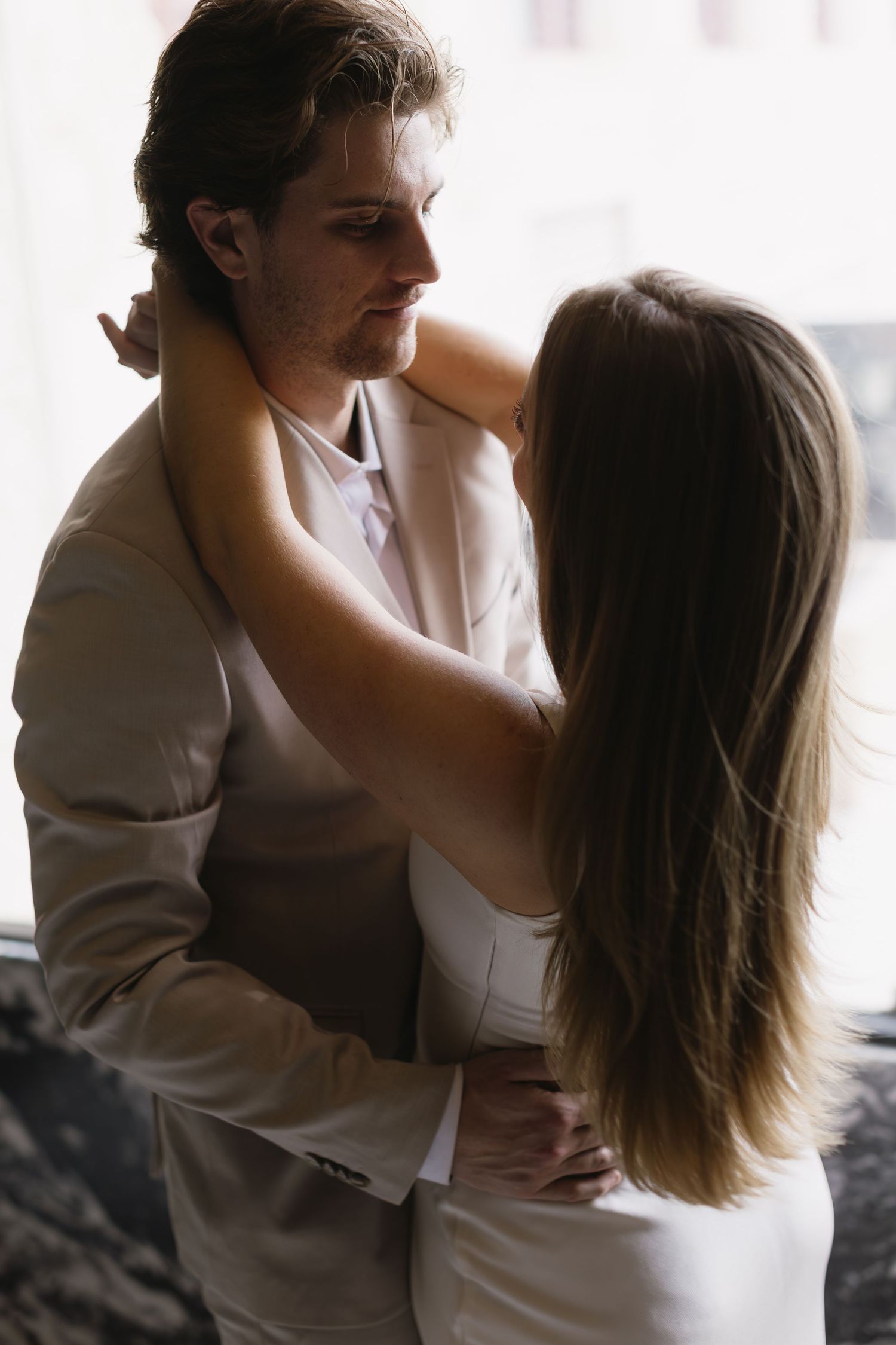 A couple in beige and white formal wear share an intimate embrace in soft lighting.