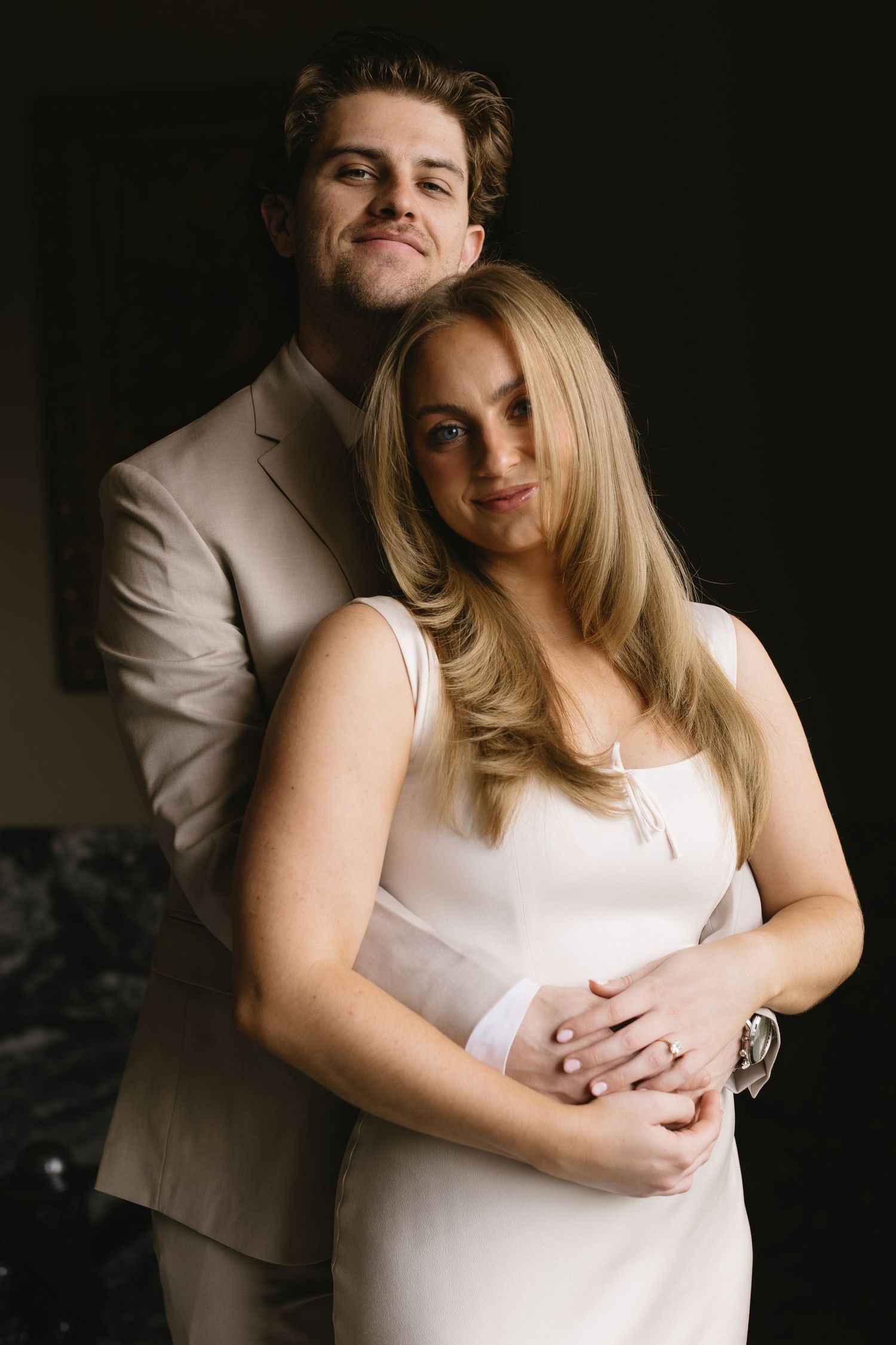 An intimate portrait of a couple in white and beige against a dark background.