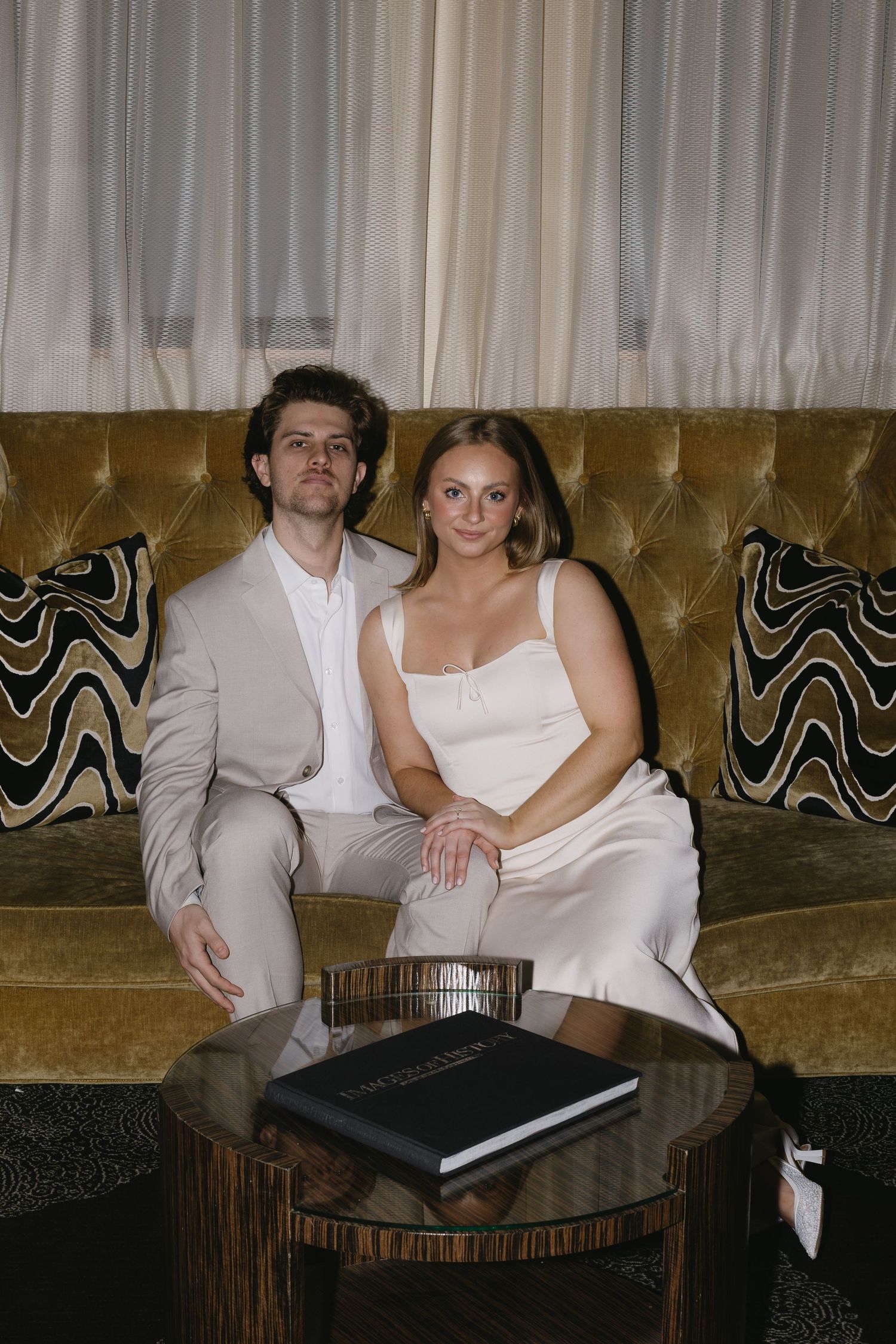Couple in formal attire relaxes on vintage velvet couch.