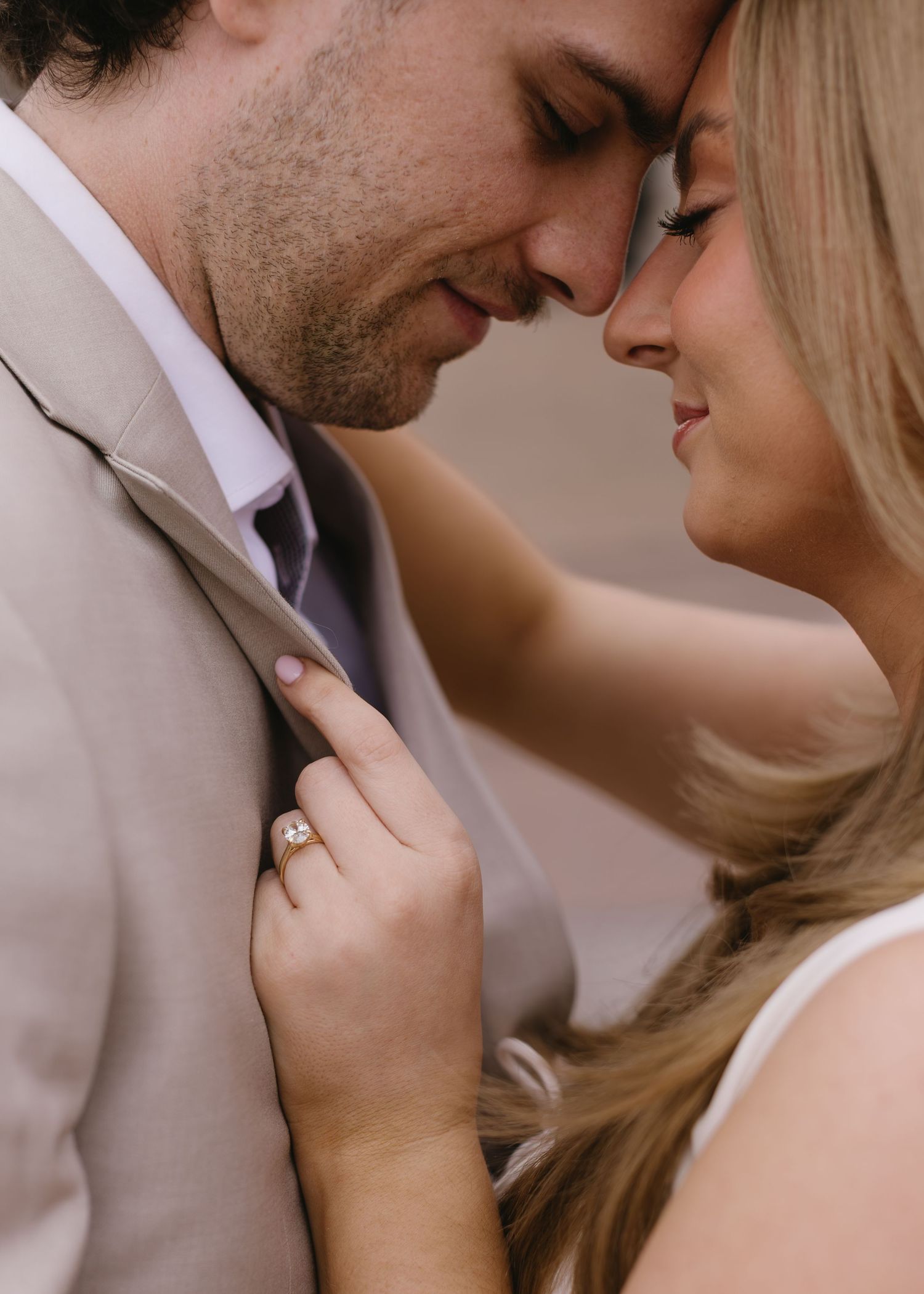 A romantic couple shares an intimate moment in matching beige and white formal attire.
