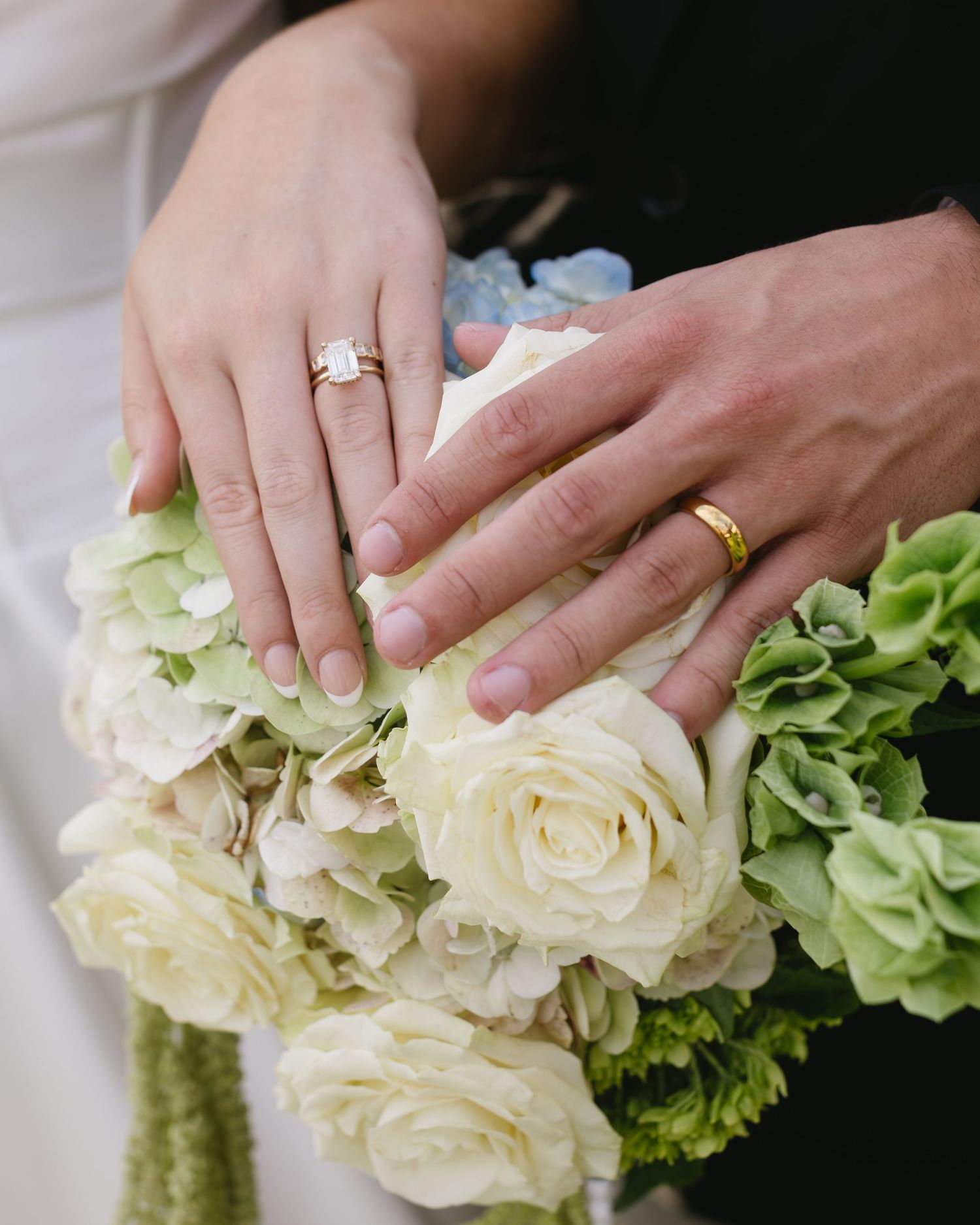 Close-up view of hands delicately arranging white roses and green hydrangeas in a floral wedding arrangement.