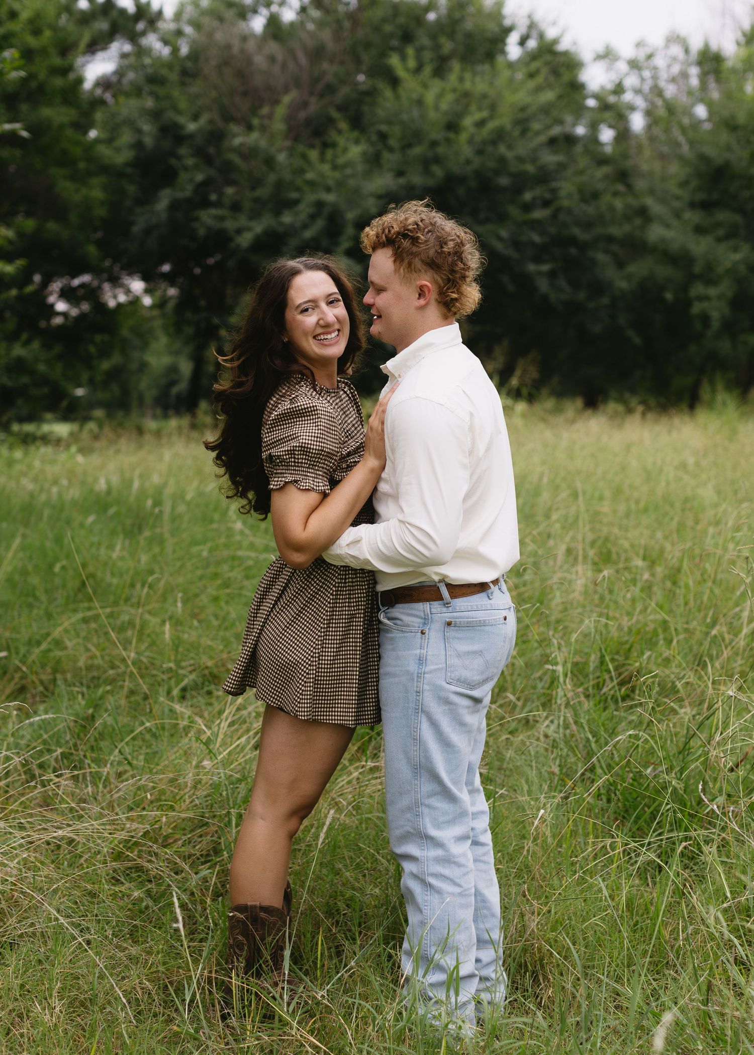 Loving couple dances in a sunlit meadow with tall grass and trees in the background.