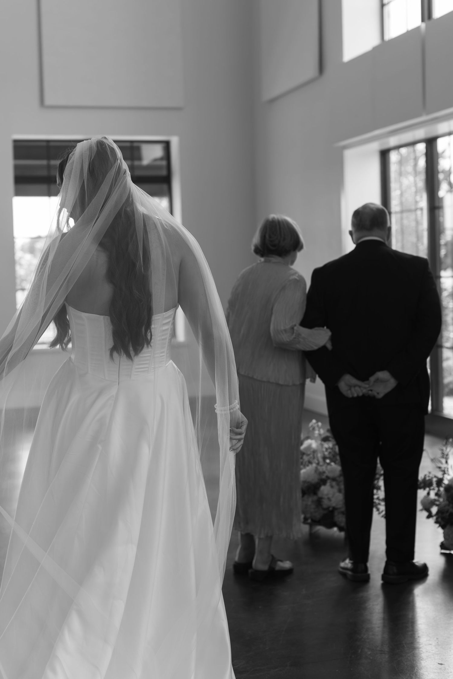 Silhouettes of wedding guests and bride during an indoor ceremony.