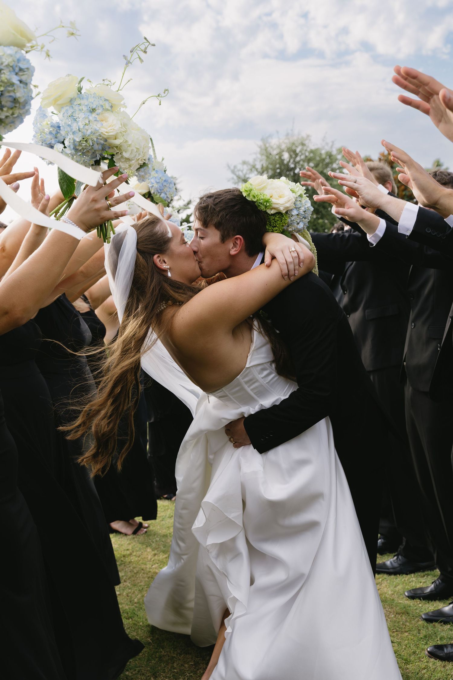 Wedding guests throw white flower petals during an outdoor celebration.