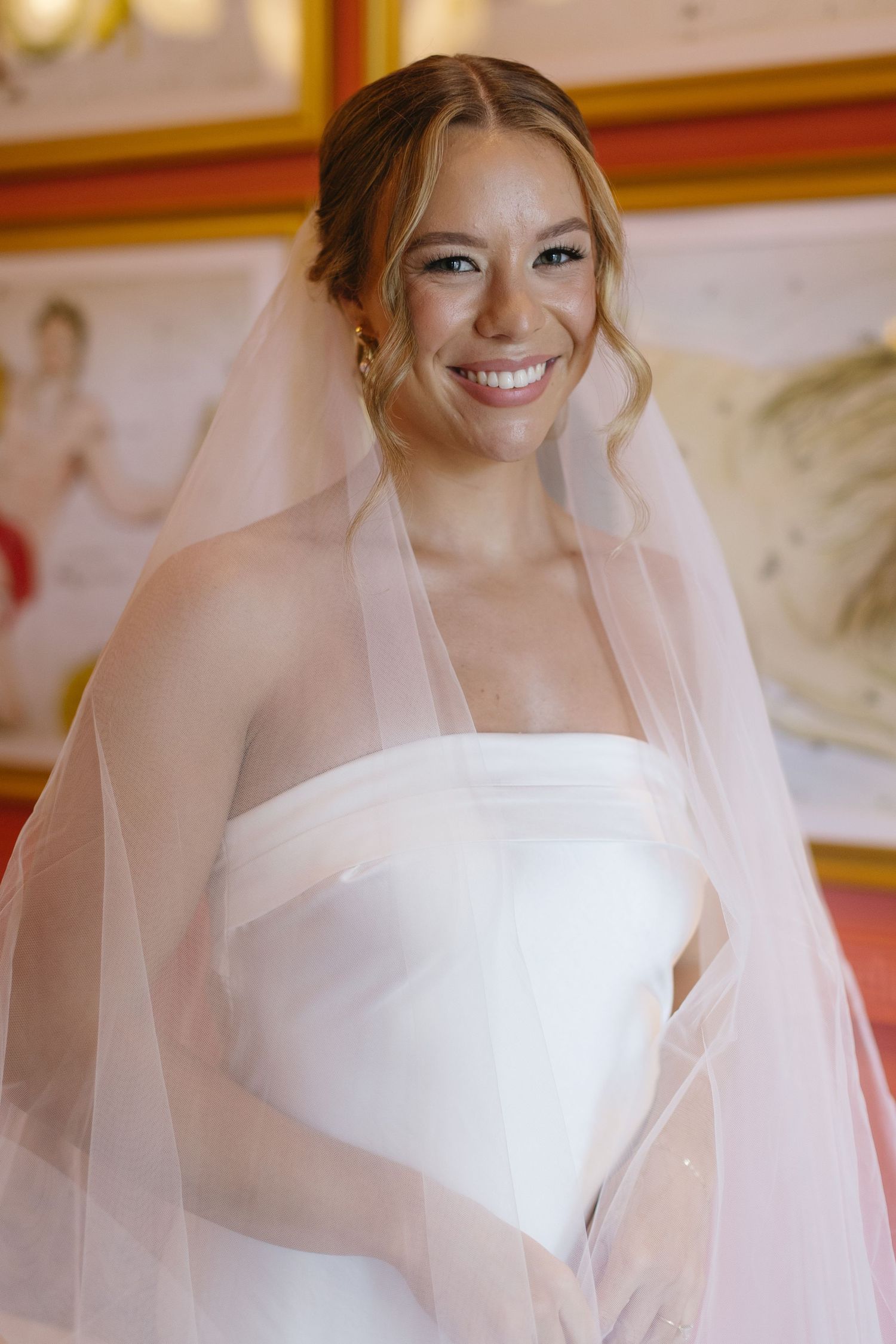 Beautiful bridal portrait featuring strapless white gown and flowing veil against warm-toned background.
