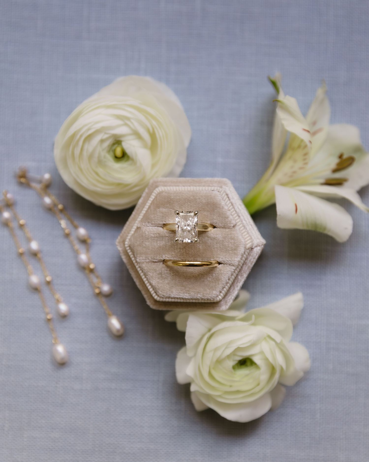 Wedding jewelry including a hexagonal ring box and pearl earrings displayed with white roses.