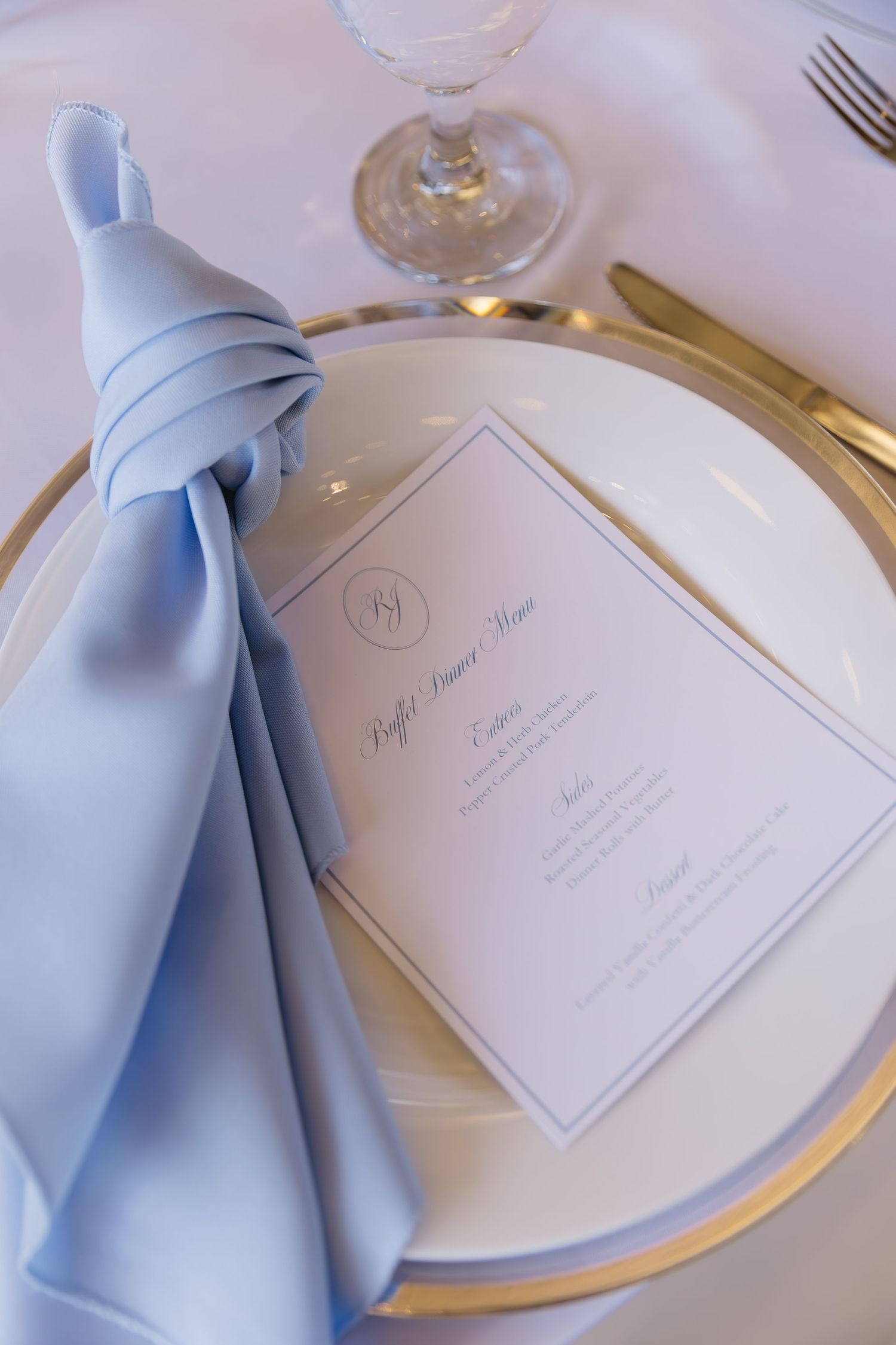 Elegant place setting with light blue napkin and menu card on gold-rimmed plate.