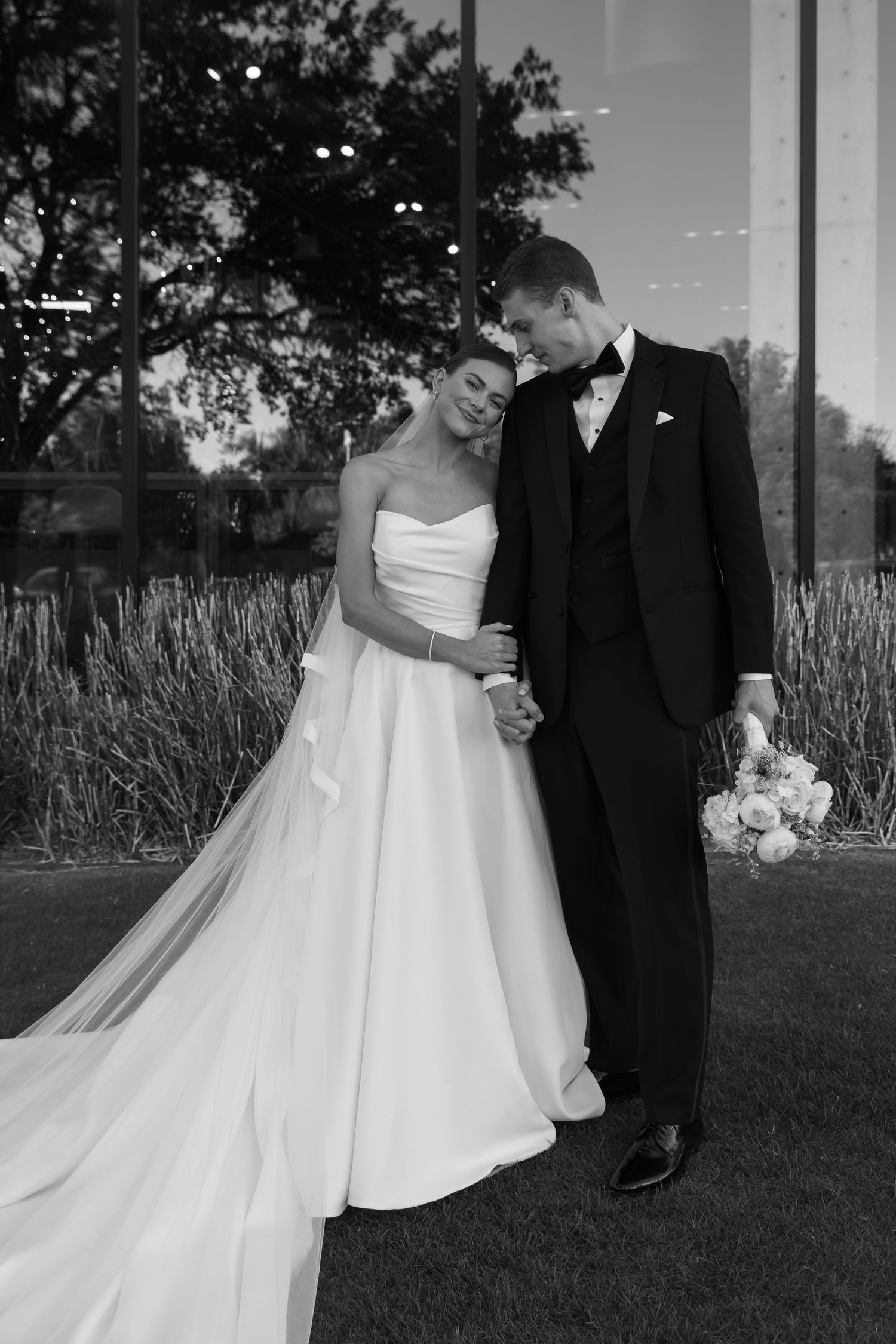 An intimate black and white portrait of newlyweds sharing a tender moment outdoors.