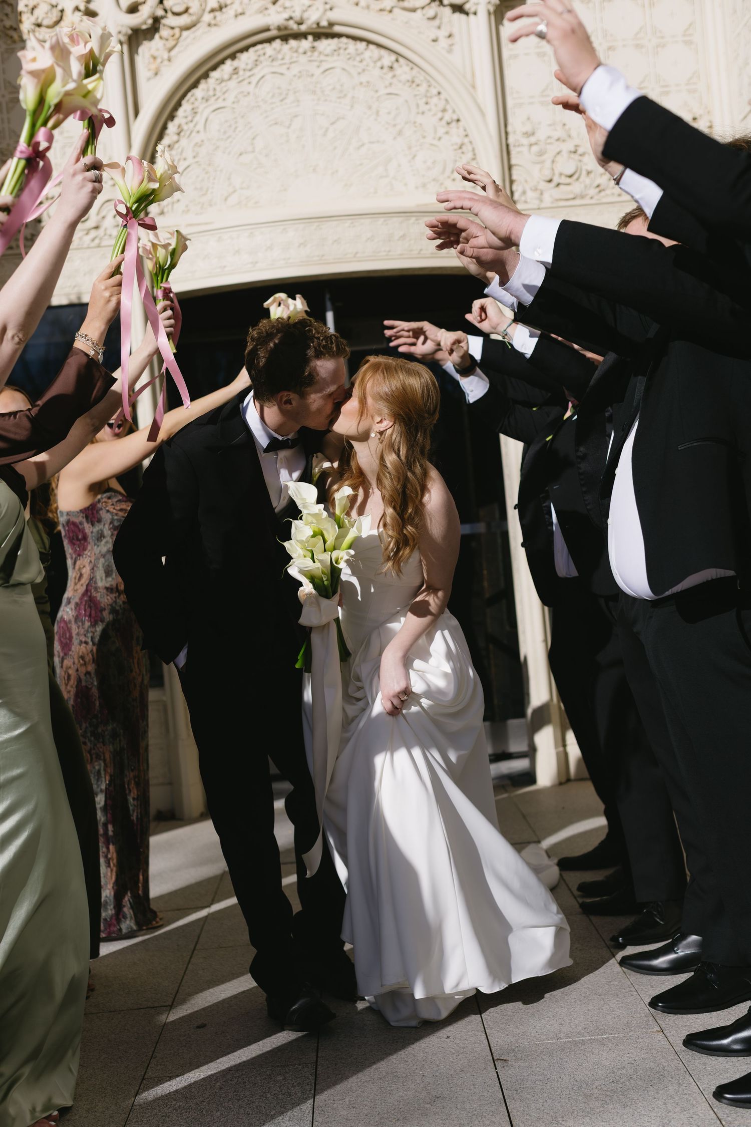Wedding party celebrating in formal attire under decorative architecture.