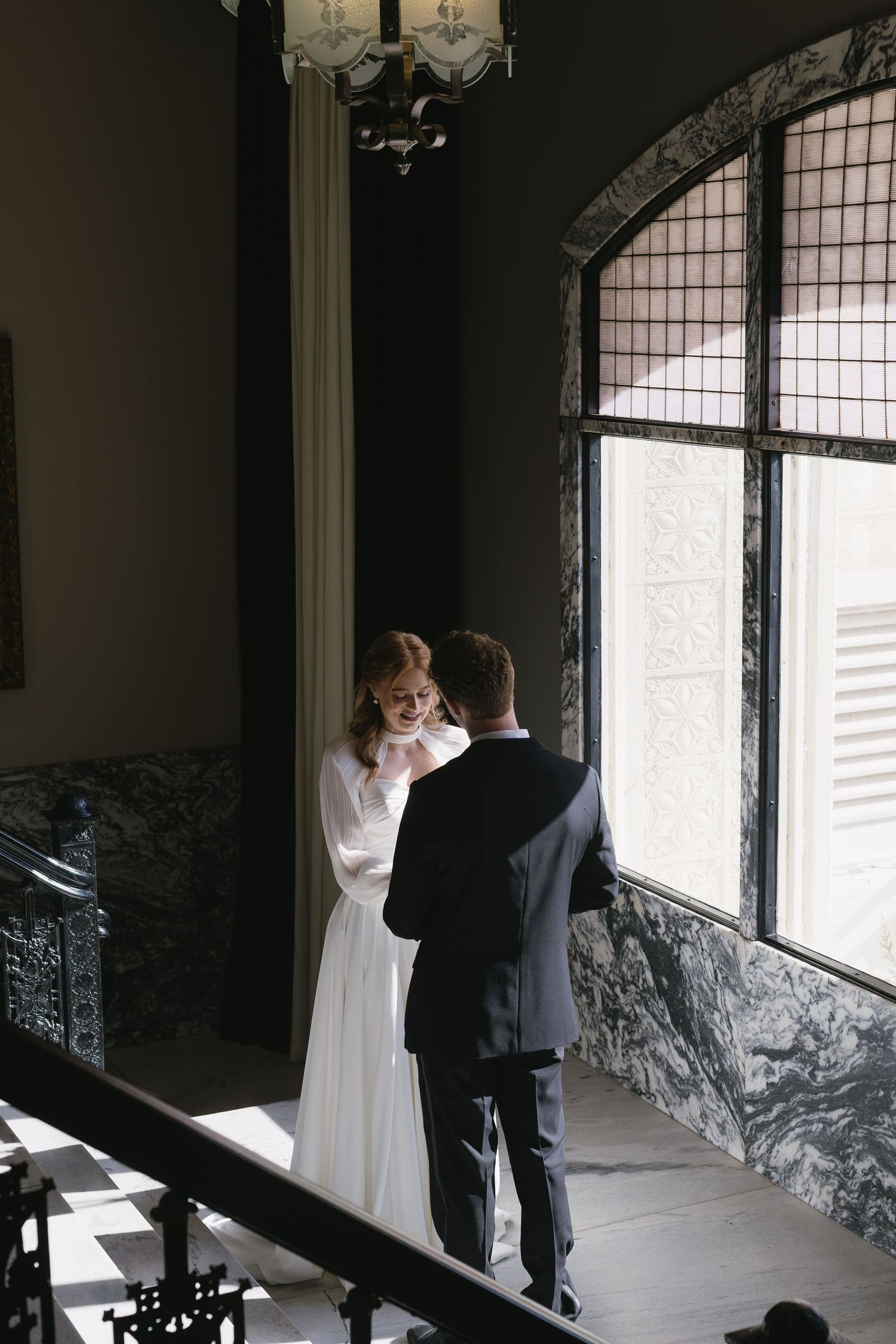 A couple shares an intimate first look moment in front of a window with marble walls.
