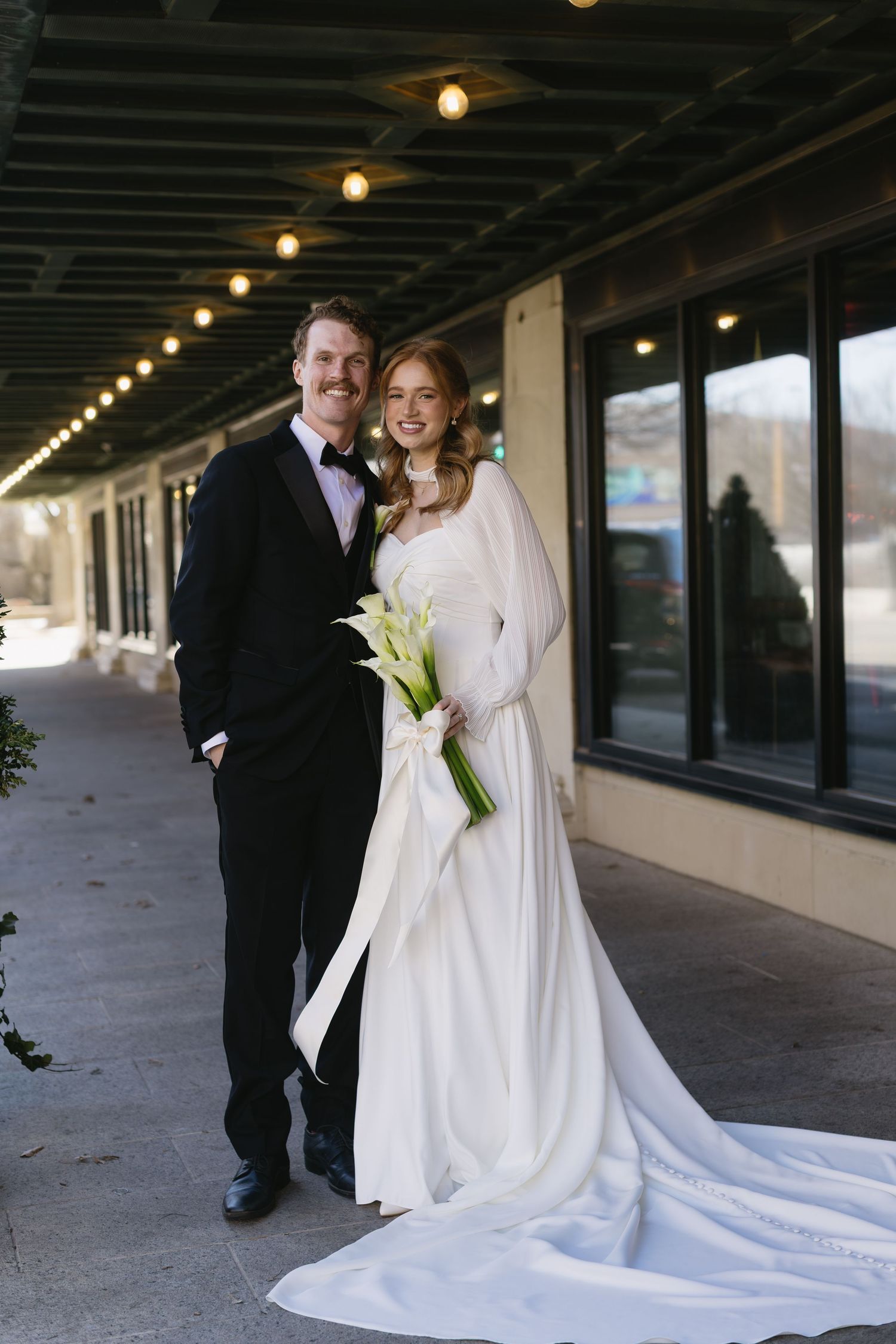 A wedding couple poses together under covered walkway with dramatic lighting.