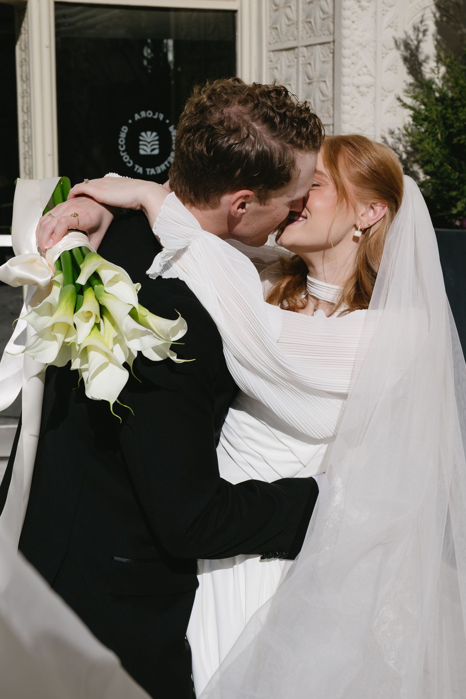 Romantic wedding moment with white calla lily bouquet against textured wall.