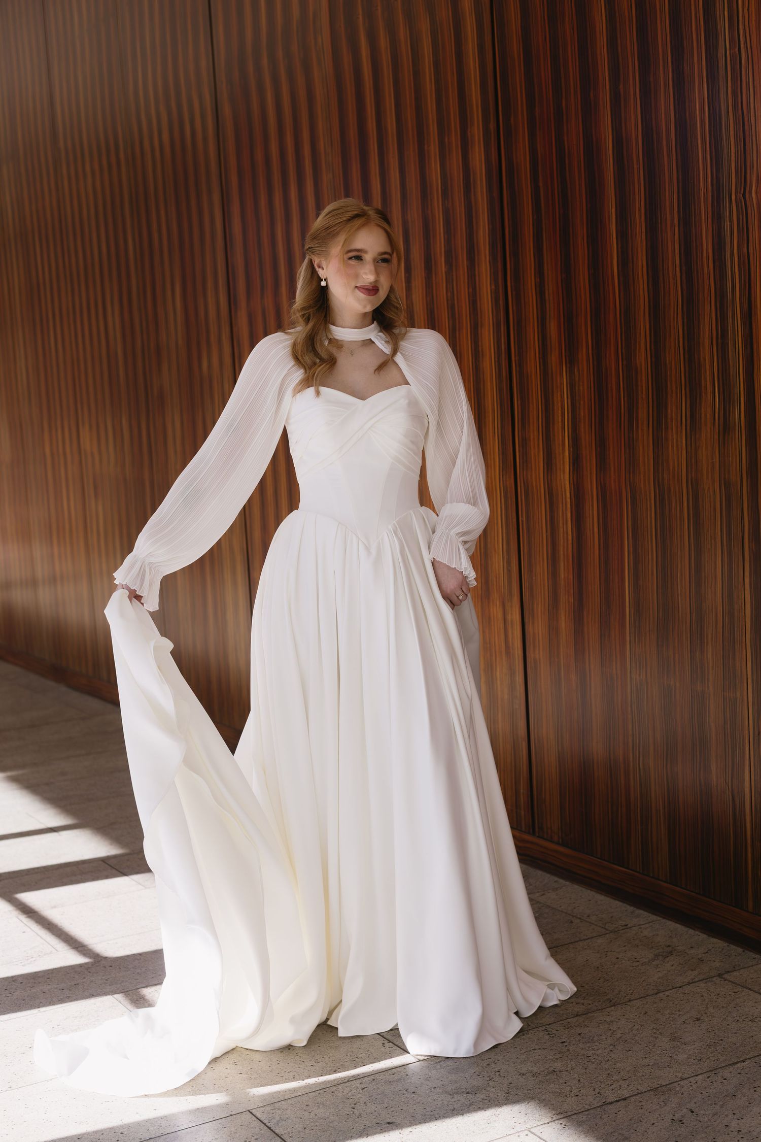 Elegant white wedding dress with flowing fabric and dramatic lighting against a wood paneled wall.