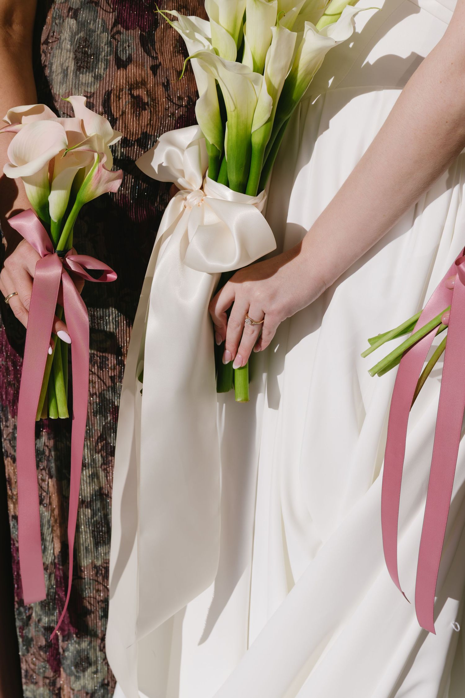 Row of bridesmaids holding white calla lily bouquets with pink ribbons.