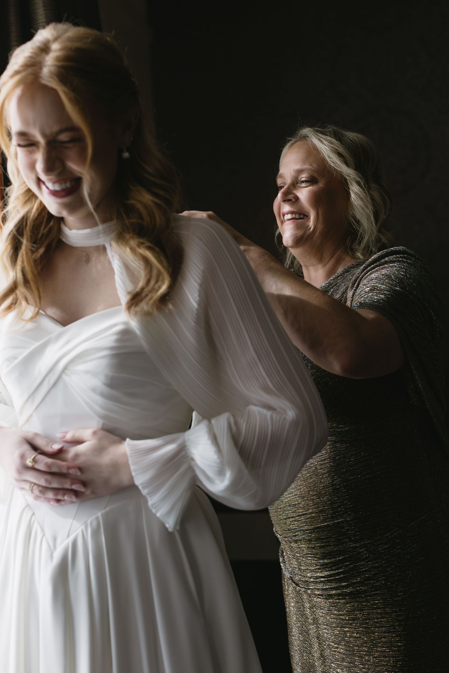 Candid getting ready moments between bride in white dress and attendant in sparkly gown.