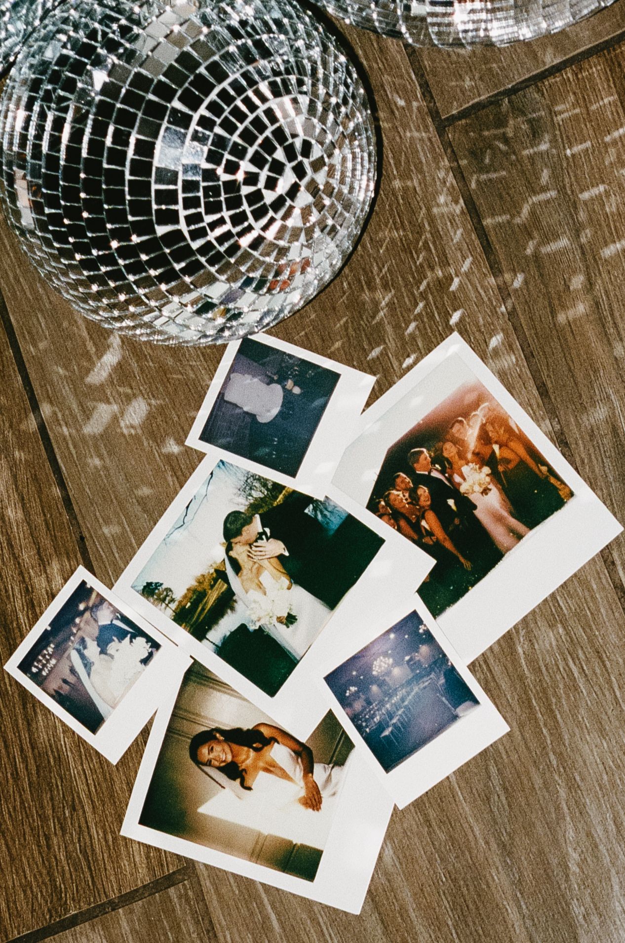 Polaroid photographs scattered beneath a reflective disco ball on a wooden floor.