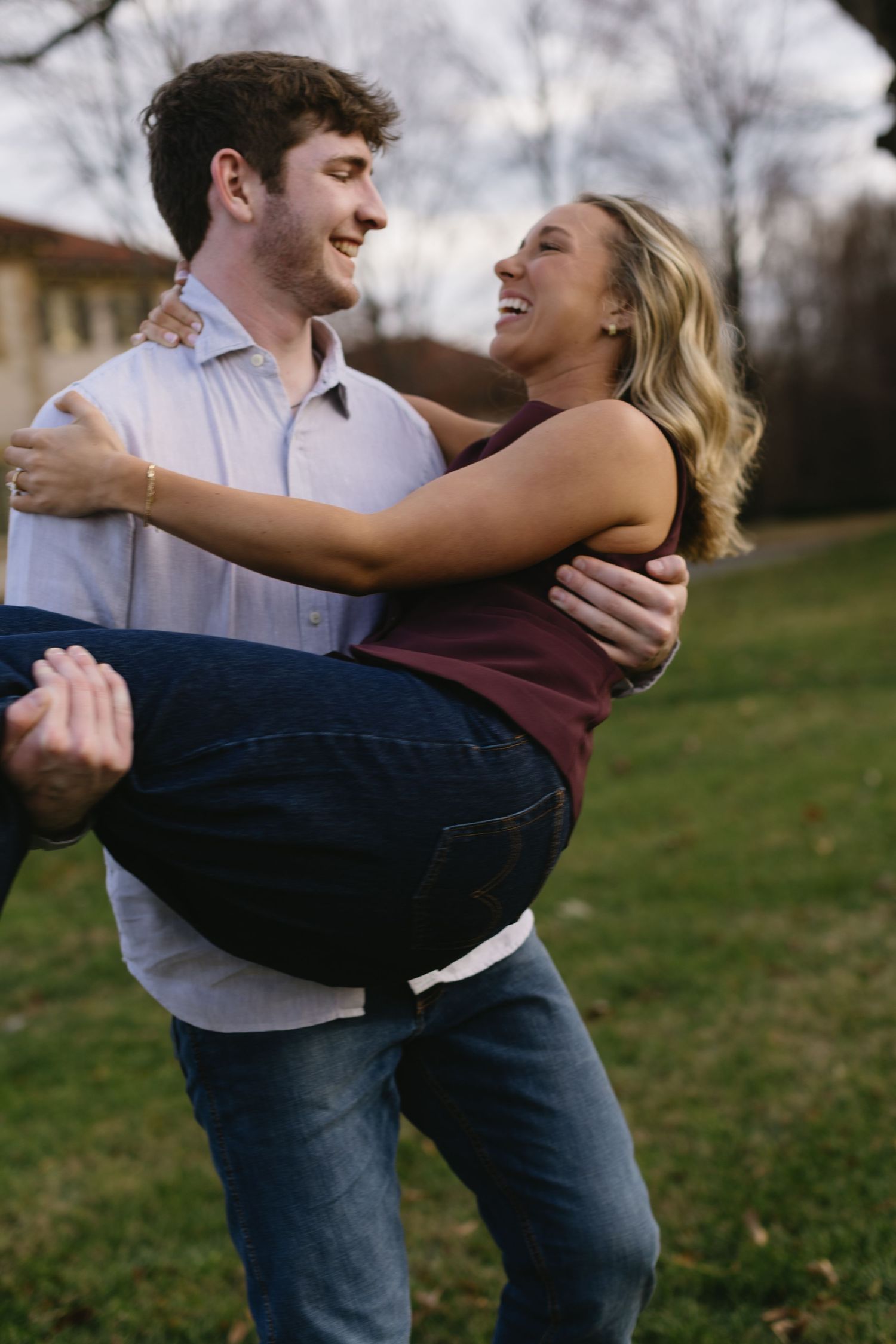 Playful couple spins and dances together in a grassy field during a romantic photo shoot.