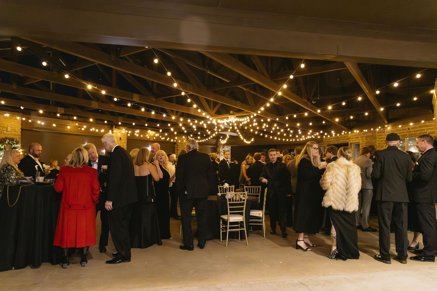 Wedding reception space with hanging string lights and guests mingling in formal attire.
