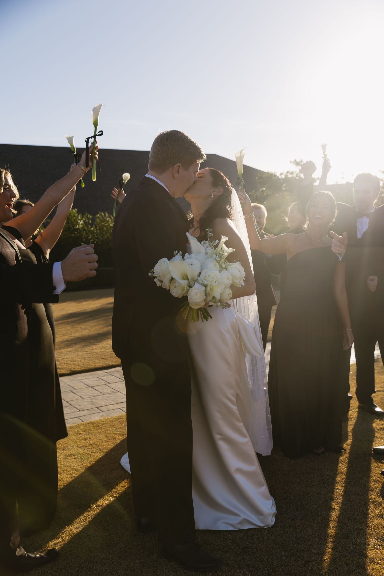 Couple embraces during sunset at outdoor wedding ceremony with guests in formal attire.