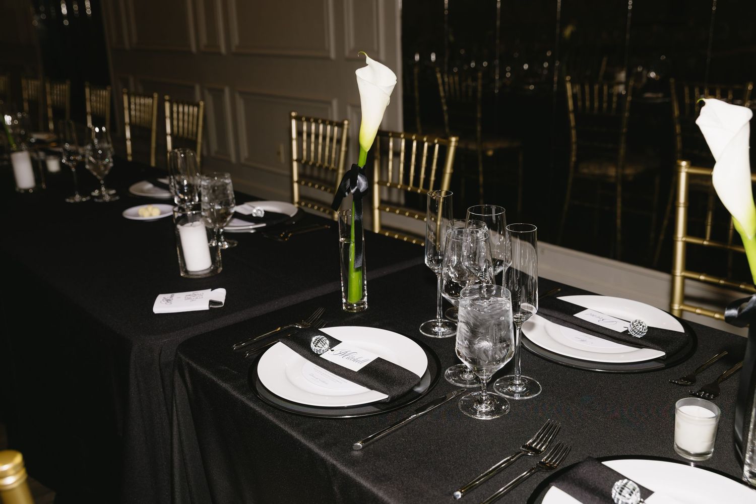 Elegant table setting with black tablecloth, white plates, and tall calla lily centerpiece.